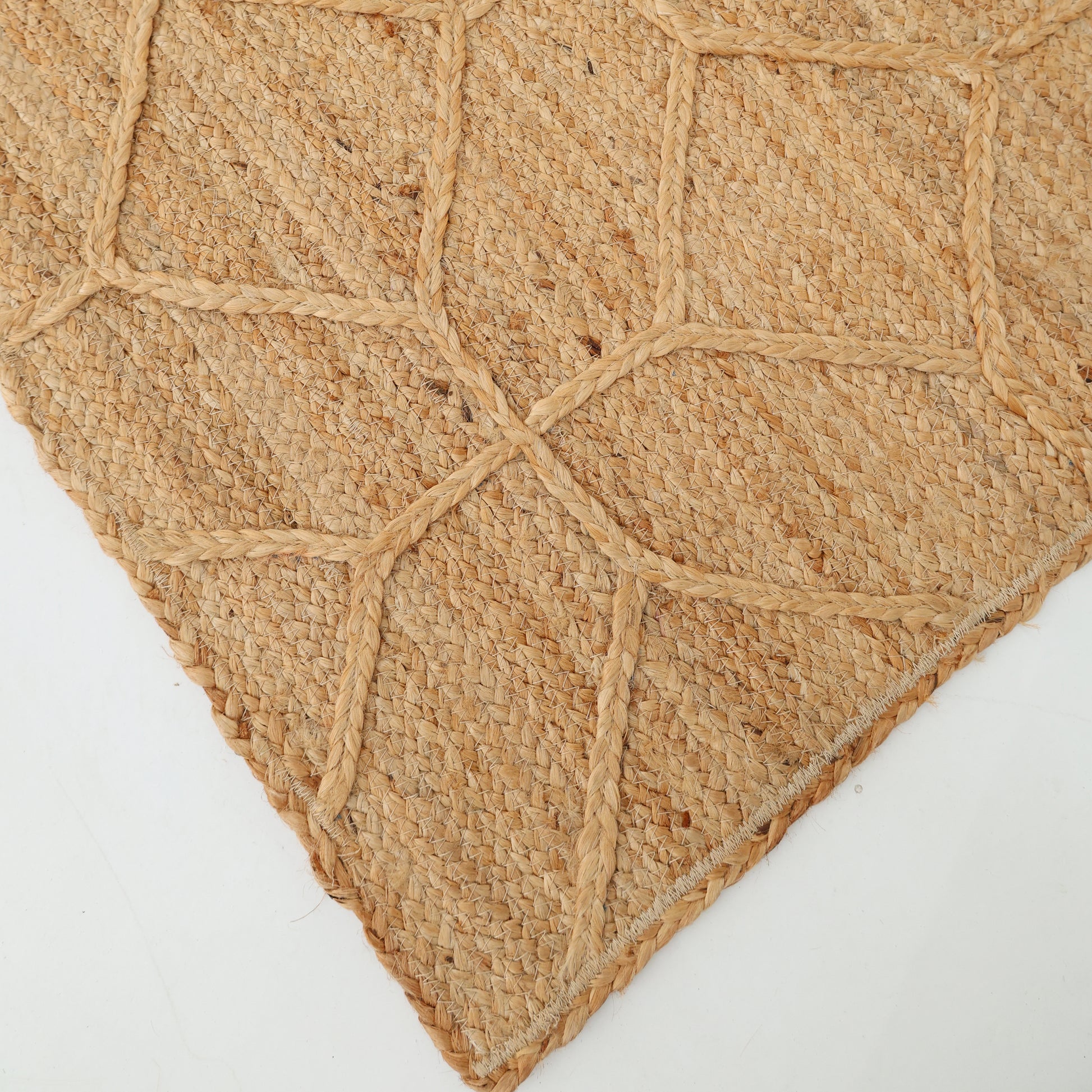 Close-up of the RAMSHA HOME Natural Color Dining Room Jute Area Braided Rug - BR 076, featuring textured, diamond-shaped raised braids. This stylish jute rug is perfect for modern interiors and is shown on a white surface.