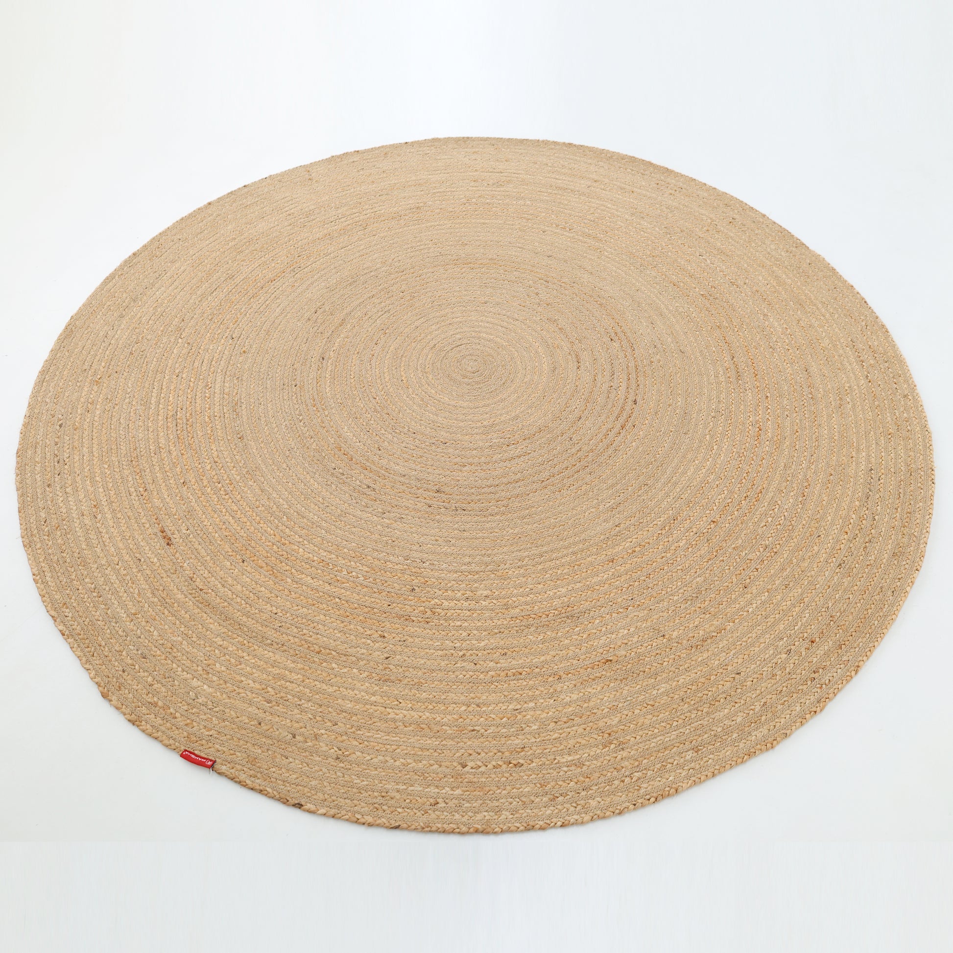 The Luxurious Handmade Home Decor Jute Rug Circle - BR 088 by RAMSHA HOME, in light beige with a woven design and a small red tag on the edge, is displayed against a plain white background.