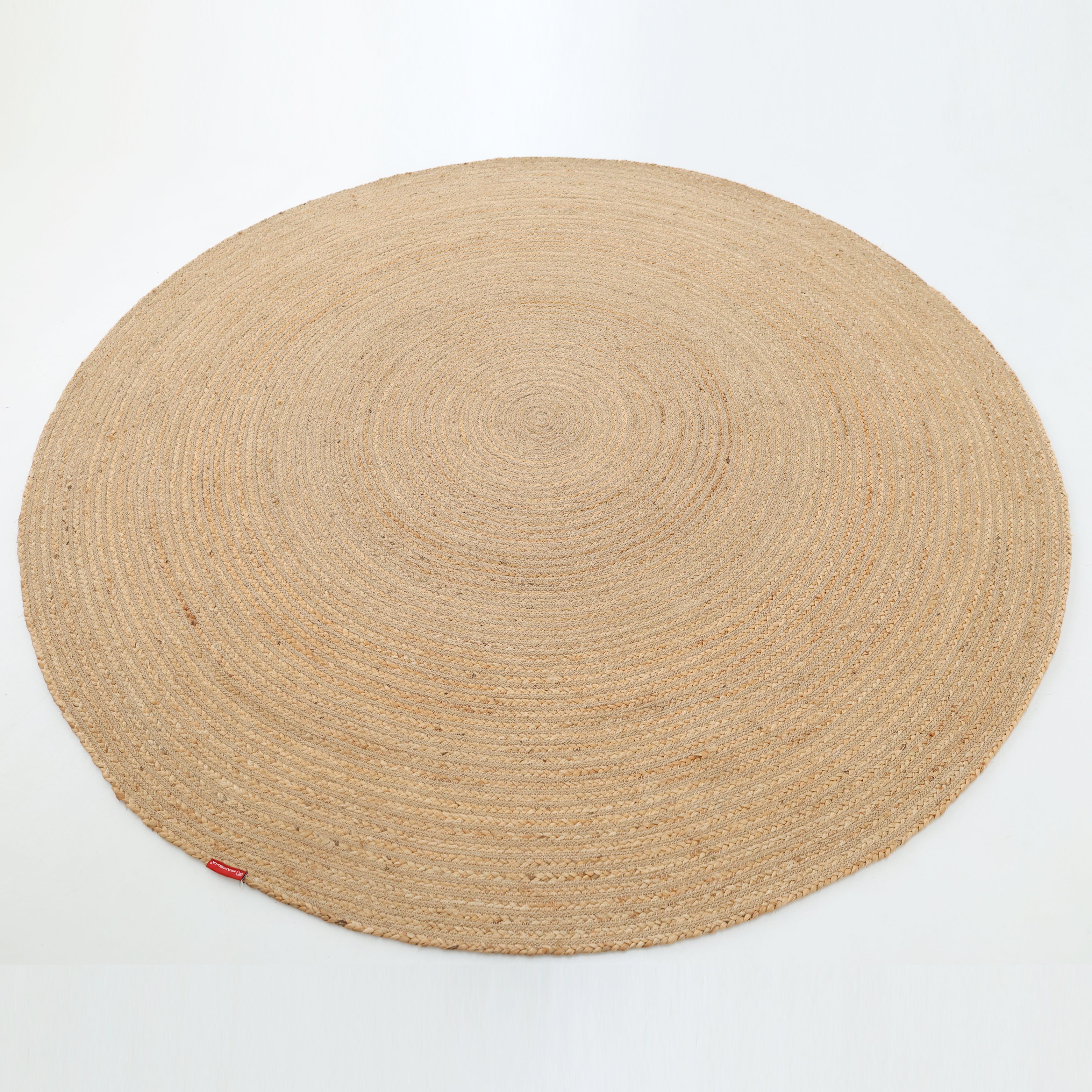 The Luxurious Handmade Home Decor Jute Rug Circle - BR 088 by RAMSHA HOME, in light beige with a woven design and a small red tag on the edge, is displayed against a plain white background.