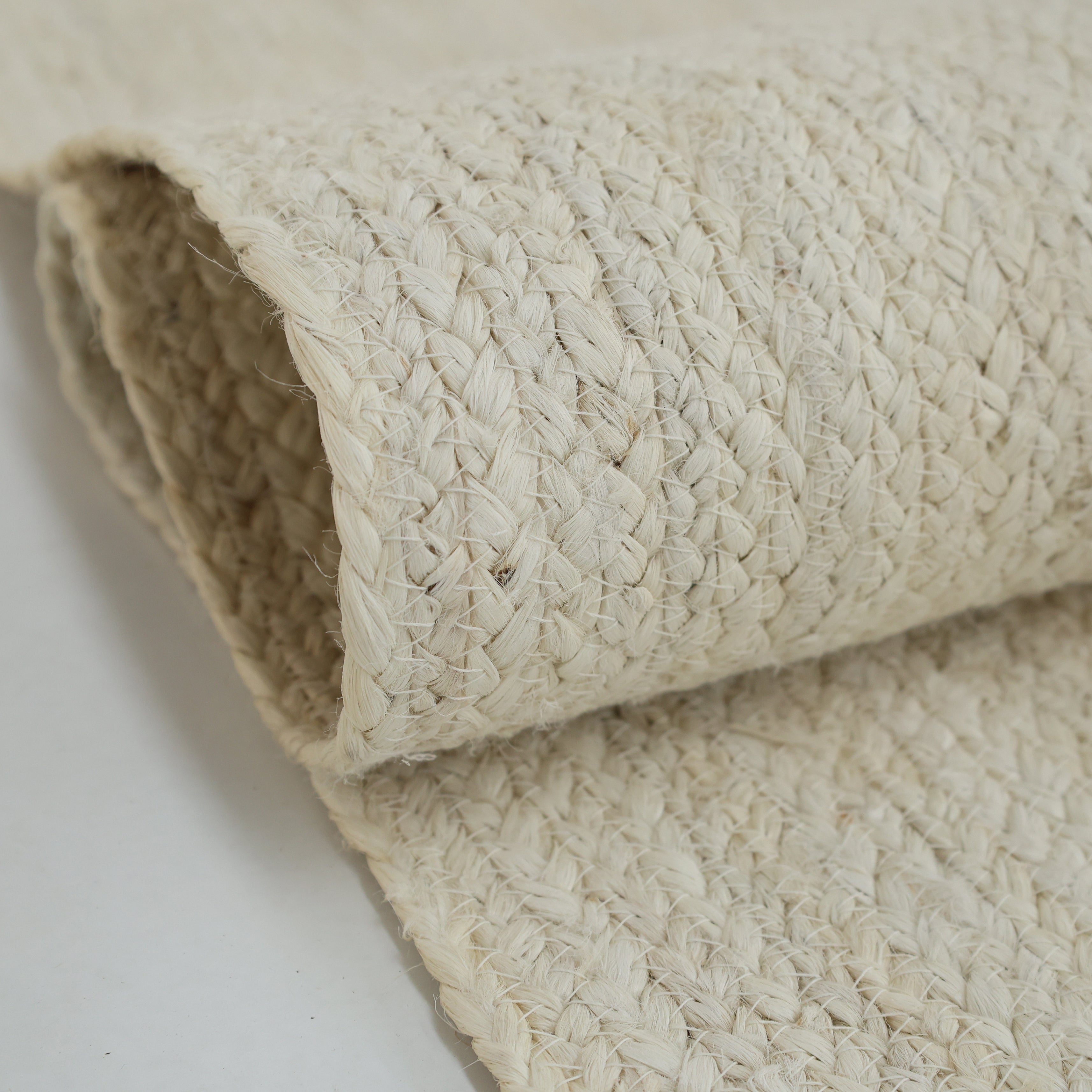 A close-up of the RAMSHA HOME Amazing Handmade Bleach Jute Braided Rug - BR 019 shows its sturdy construction, light beige color, and textured braided pattern in natural woven jute.