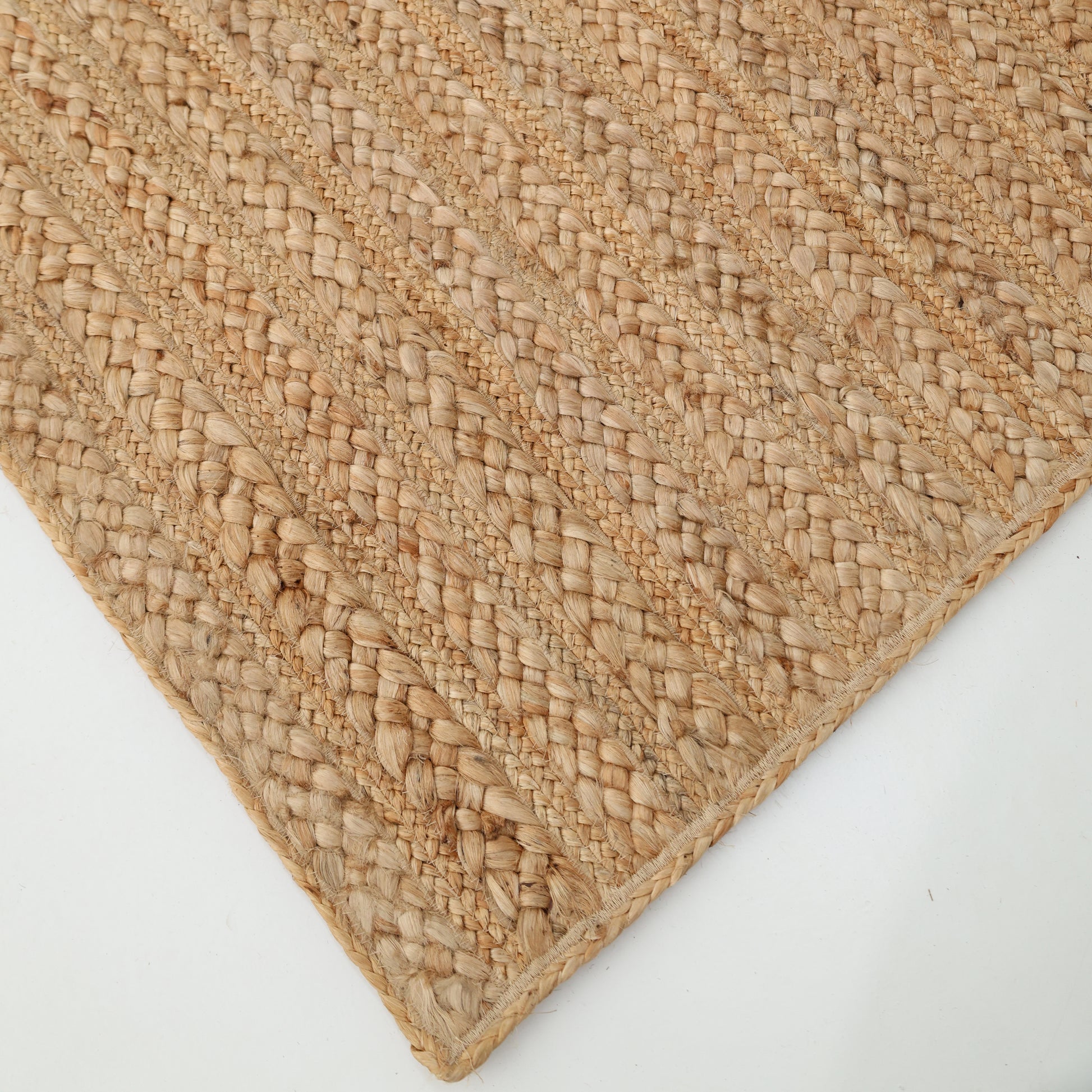 A close-up of the RAMSHA HOME Braided Jute Natural Color Handmade Rug (BR 021) highlights its natural fiber texture and diagonal patterns, elegantly displayed on a white surface.