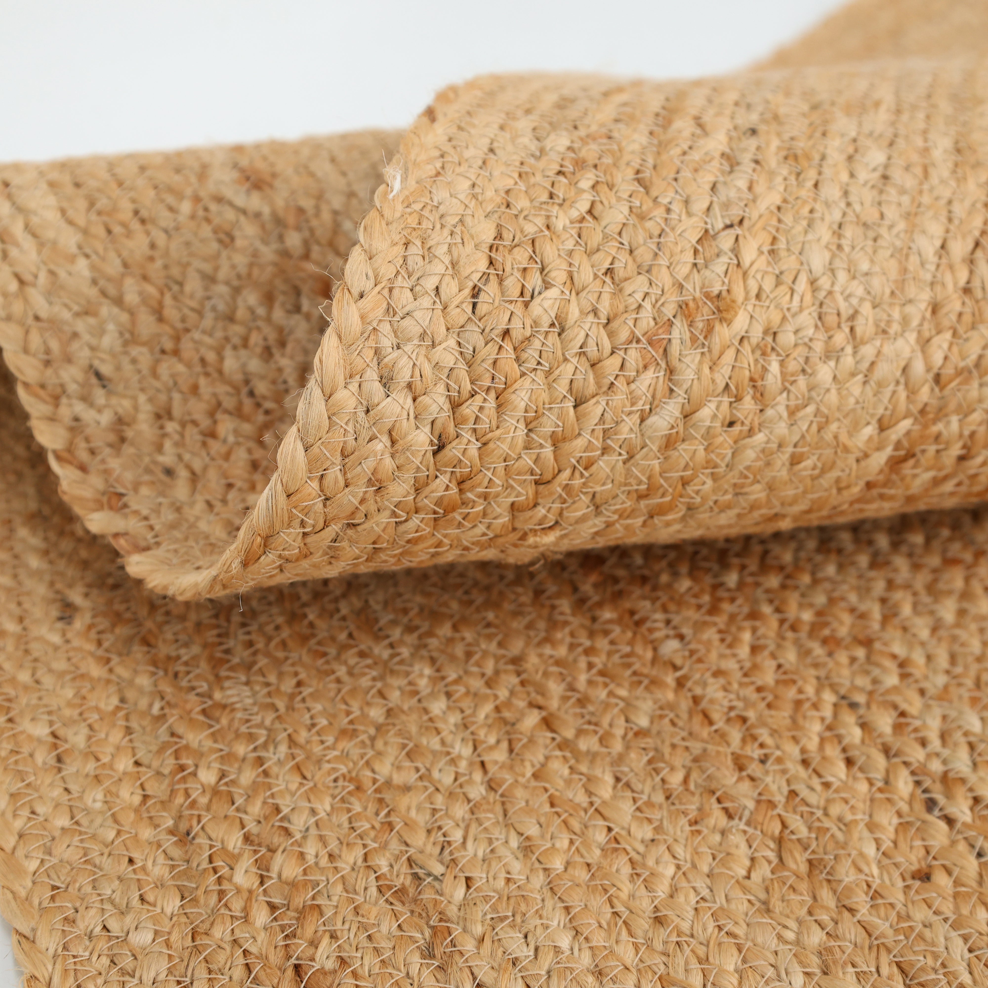 A close-up of the RAMSHA HOME Handmade Jute Braided Rugs for Living Room BR-016 highlights its natural beige fibers, textured surface, and a neatly rolled corner.