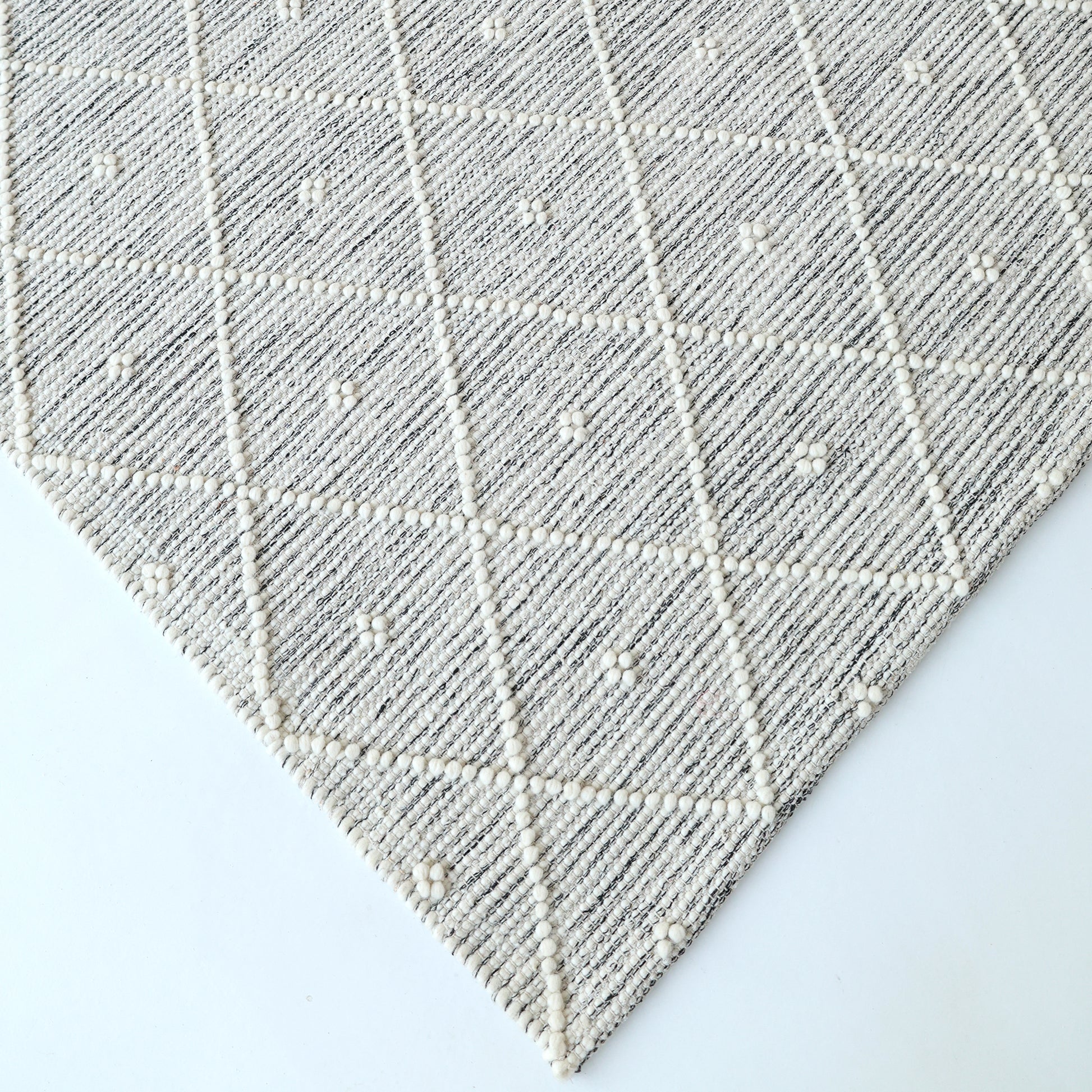 A close-up of the RAMSHA HOME Natural & White Color Woven Rug (SRN-012), featuring a subtle diamond and dot pattern with raised textured lines and small tufts, displayed on a white surface.