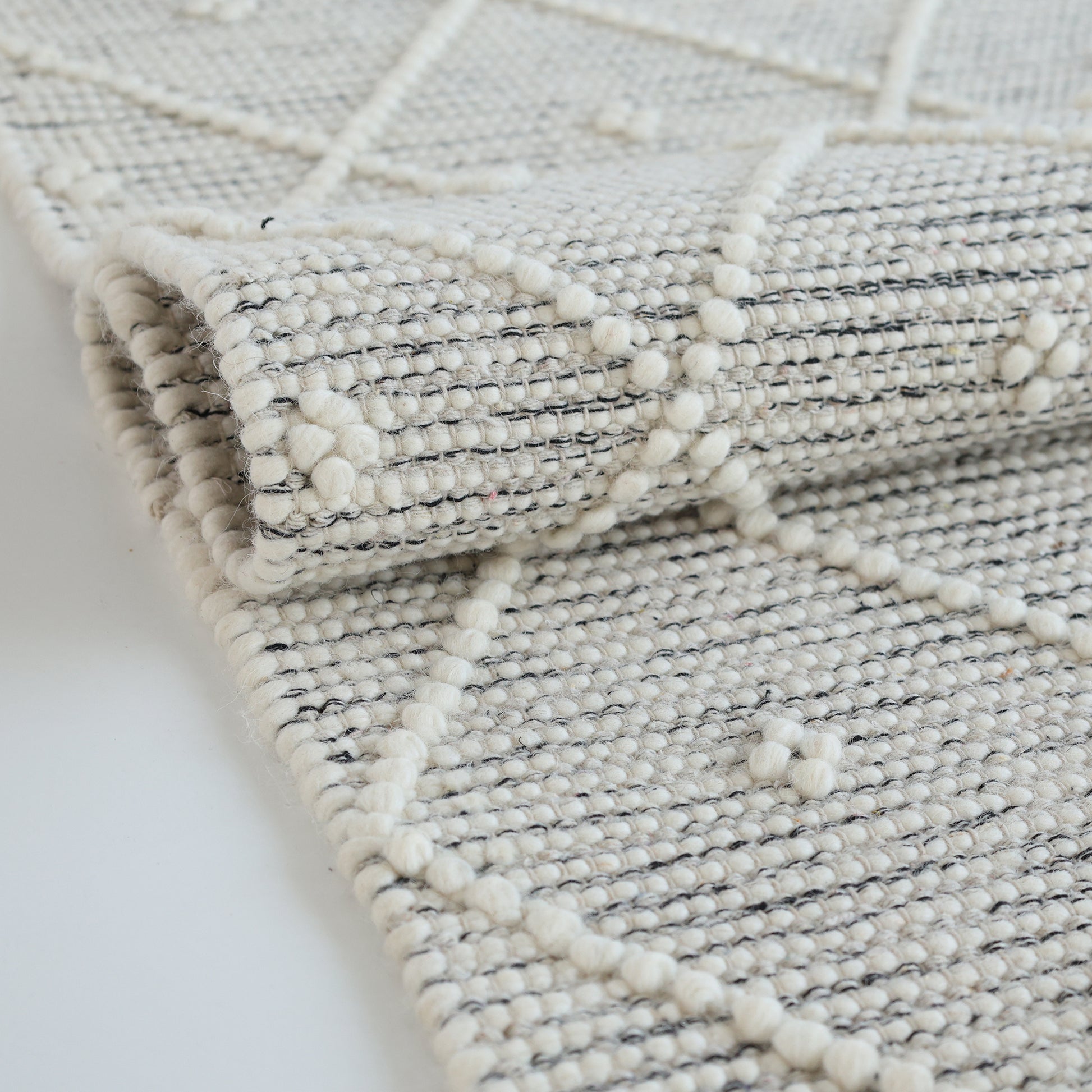 A close-up of RAMSHA HOME’s Natural & White Color Woven Rug SRN-012 shows its hand-tufted texture and raised diamond and dot pattern in light neutral tones. The detailing of this floor rug is clearly visible.