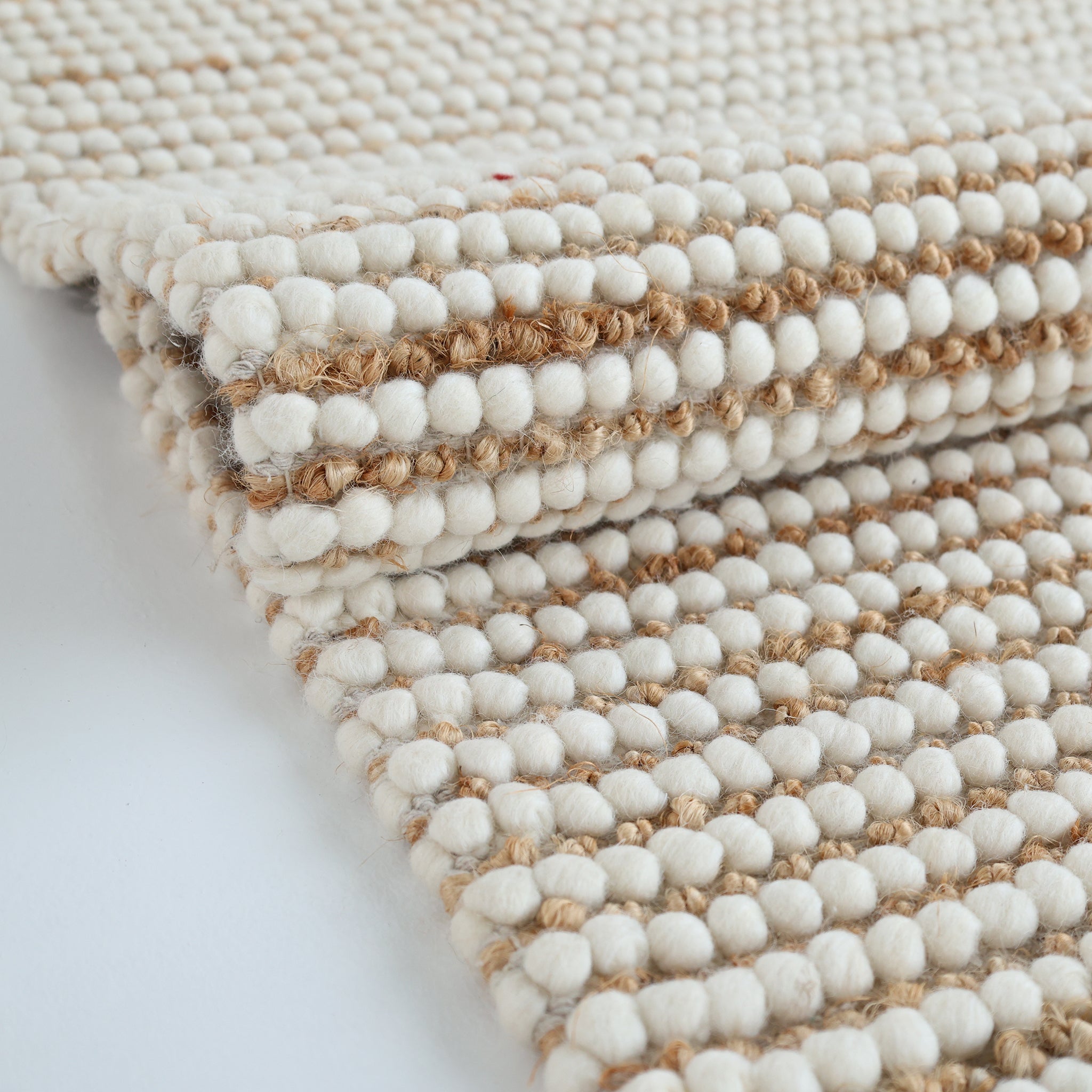A close-up of the RAMSHA HOME Solid Textured Loop Pile Woven Rug For Home Decor SRN-027, crafted from natural fibers with cream and tan woolen knots in a textured pattern on a white background.