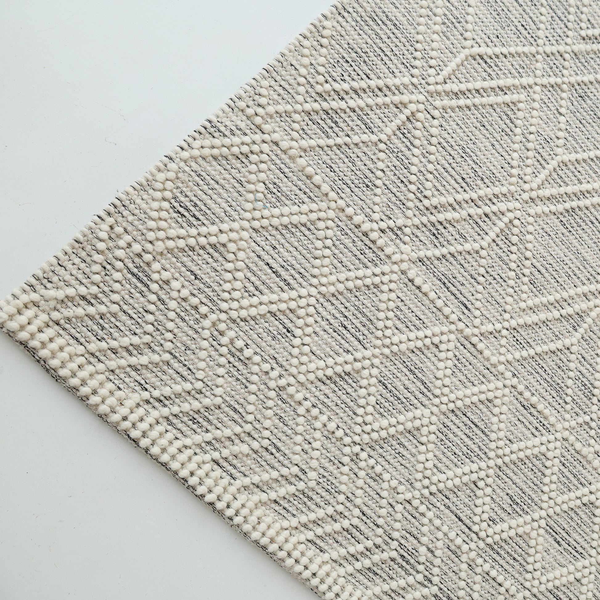 A close-up of the RAMSHA HOME Wool & Cotton Living Room Woven Rug SRN-019 in cream, featuring raised dots and angular diamond patterns, is shown diagonally on a white surface.