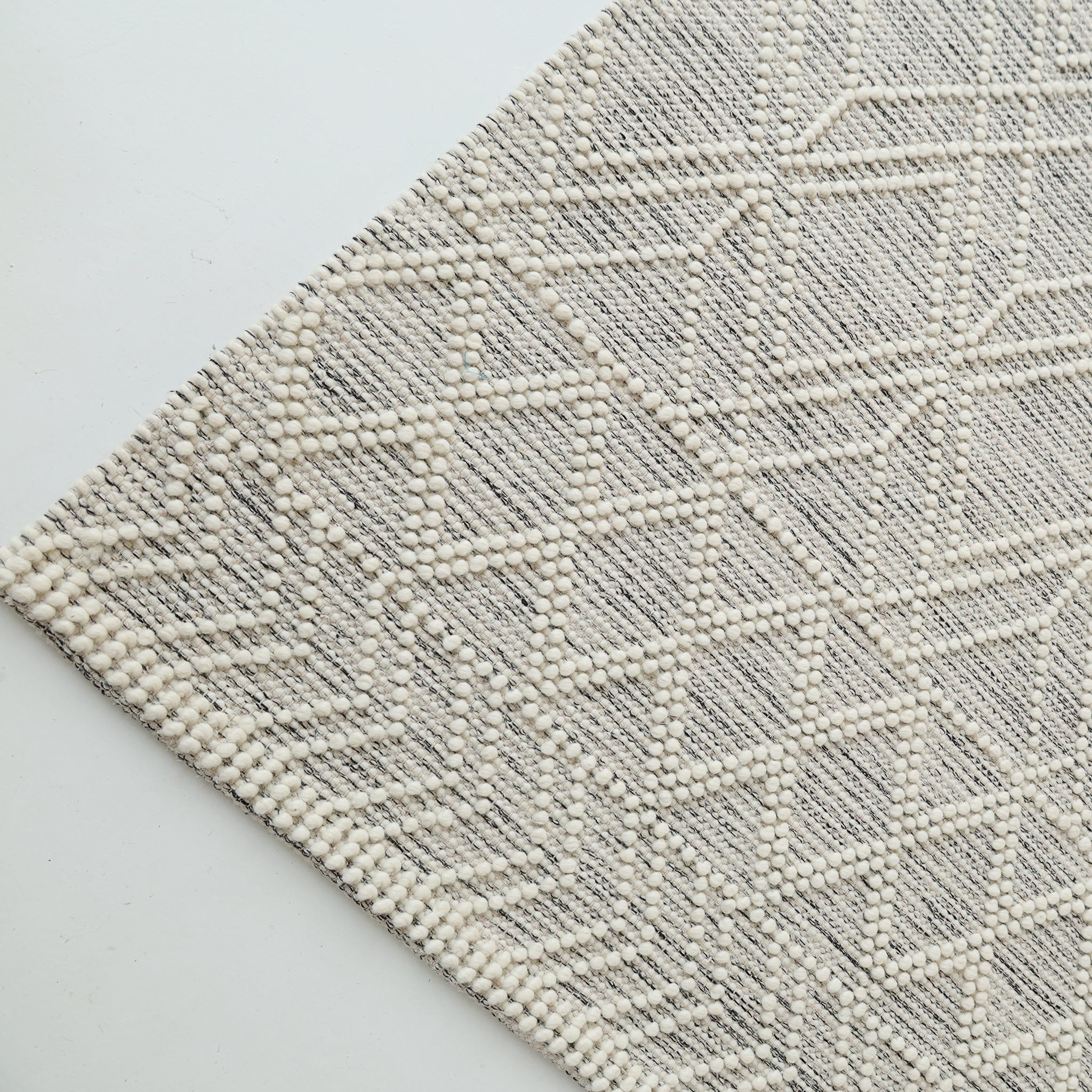 A close-up of the RAMSHA HOME Wool & Cotton Living Room Woven Rug SRN-019 in cream, featuring raised dots and angular diamond patterns, is shown diagonally on a white surface.