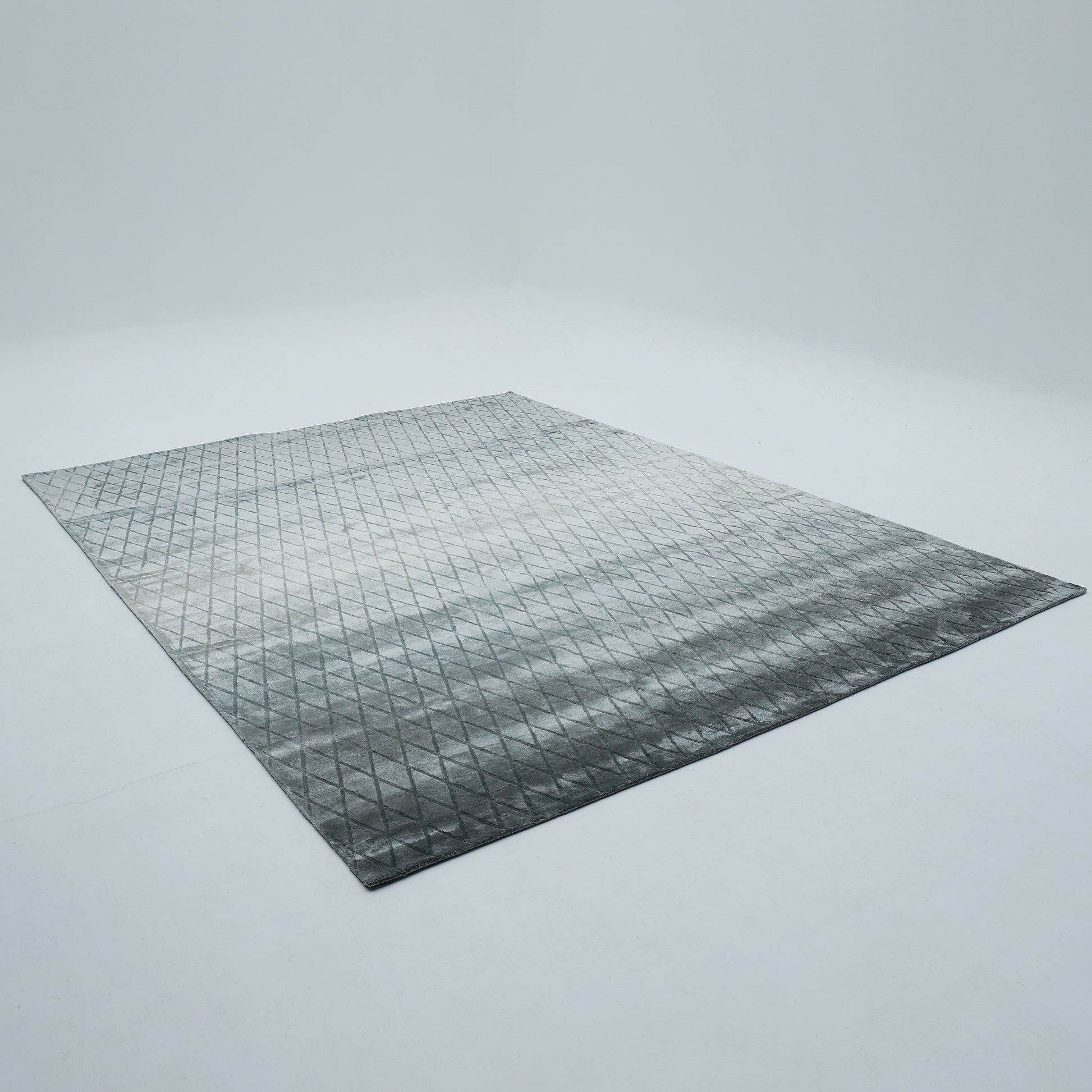 The RAMSHA HOME Steel Diamond Handmade Rug HTV 28 (300x400 cm), a large rectangular gray geometric piece with a diamond pattern, lies flat on a clean white floor in an empty minimalist room with plain white walls.