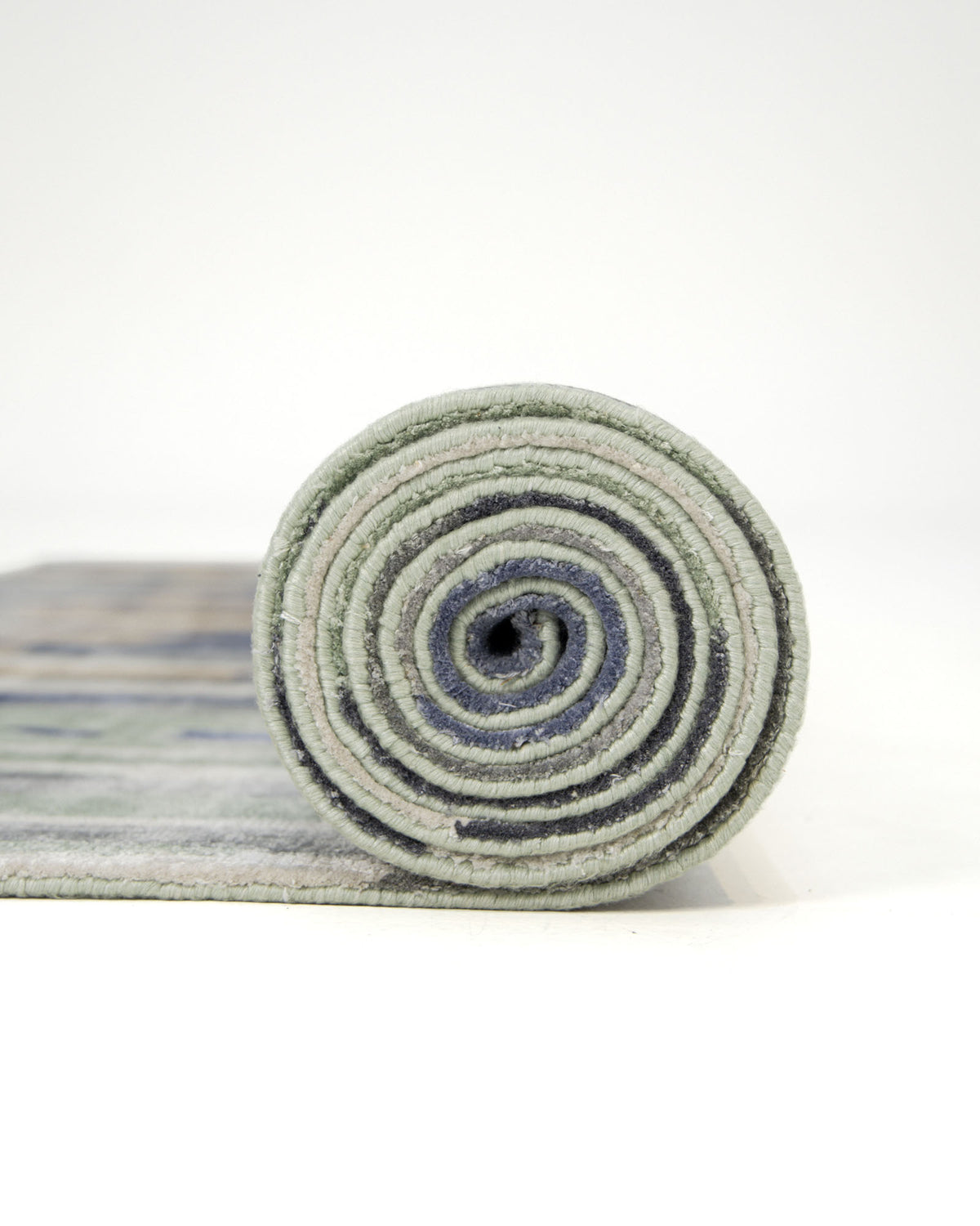 A rolled-up RAMSHA HOME Decorative Area Carpet Tencil & Cotton Multi Color HKV-09 is positioned upright on a white surface, with the hand knotted rug partially unrolled in the background.