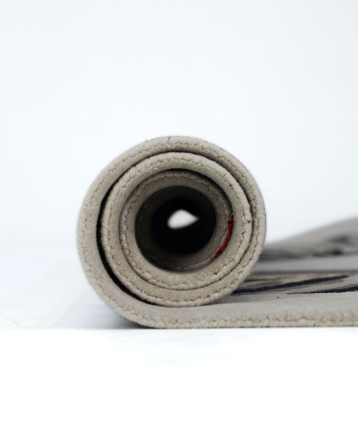 A close-up view of the Unshape Handmade Multi Color Rug HTW-82 by RAMSHA HOME, featuring visible stitching along the edge and shown rolled up against a plain white background.