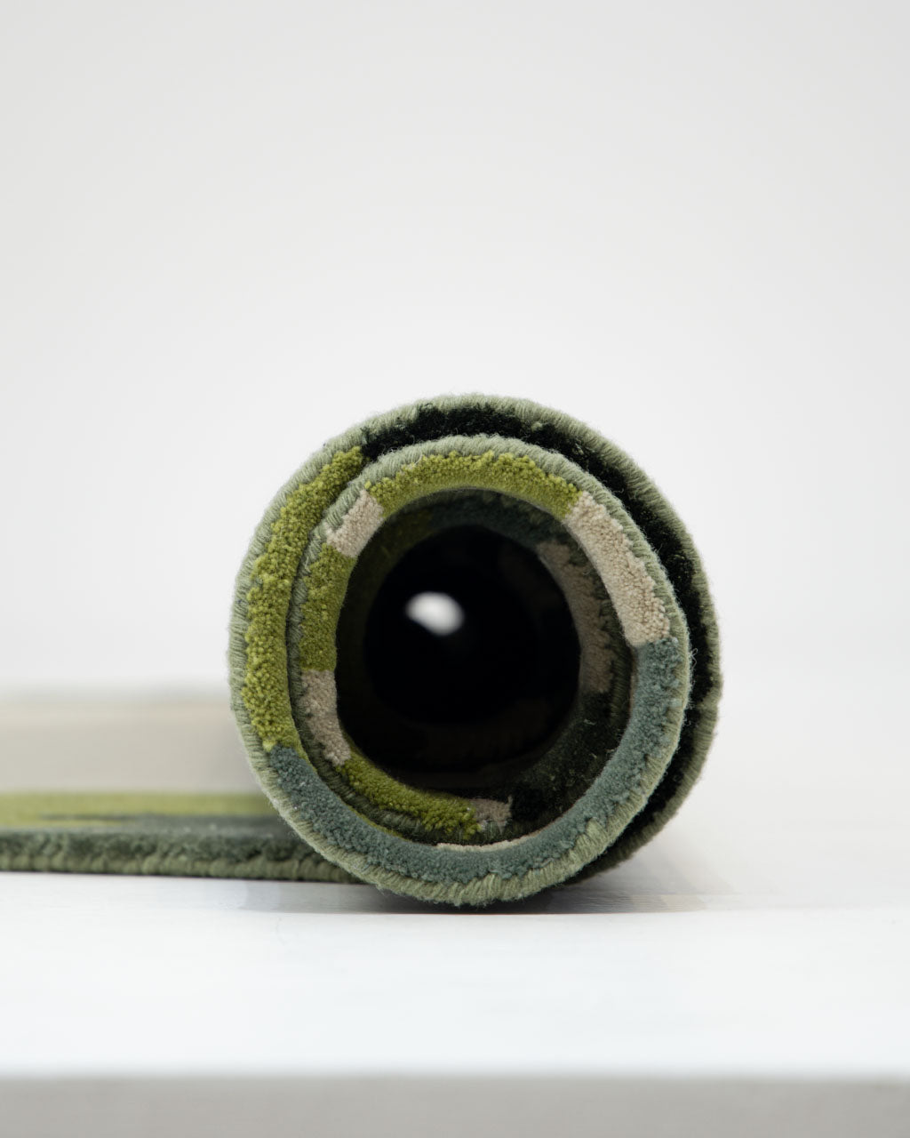 Close-up view of the RAMSHA HOME Terra Eclipse Oval Handmade Rug Accent Rug HTWV-201 in green and beige, rolled up and positioned upright on a white surface with a plain white background.