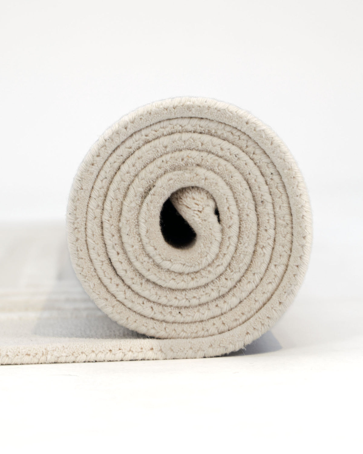 Close-up of the RAMSHA HOME Hand-Tufted Carpet For Home And Office HTWV-70, rolled up on a white surface, showcasing its minimalist design with visible spiral coils from a side view.