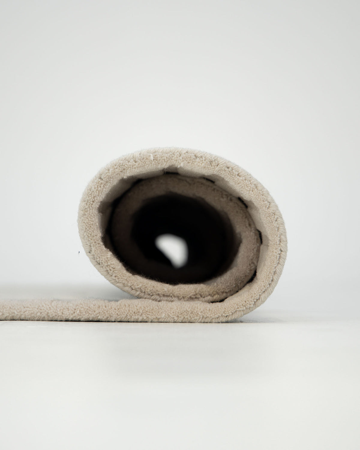 A roll of the RAMSHA HOME Home Decor Handmade Area Rug - HTW 96 in beige is partially unrolled on a white surface, with the roll positioned directly toward the viewer against a plain, light background.