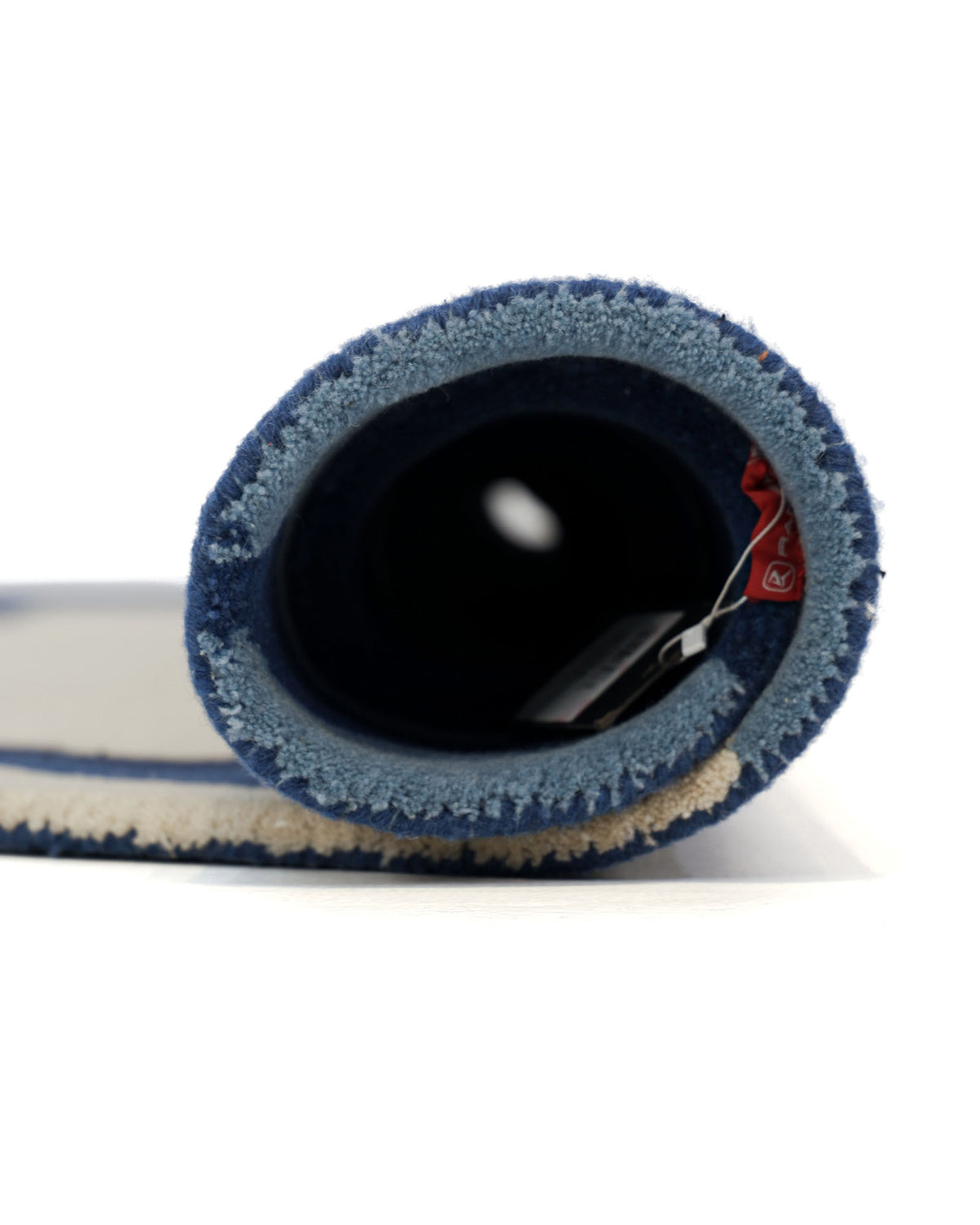 A side view of the Round Handmade Hand Tufted Carpet HTW-64 by RAMSHA HOME, rolled up with its label attached, displays the blue and beige modern design and reveals the inner circular opening.