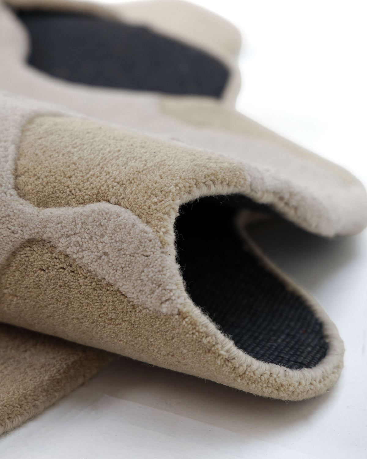 A close-up of the beige and black textured fabric of the RAMSHA HOME Contemporary Flow Area Handmade Rug HTW-153, showcasing its thick, soft, and padded appearance as it lays on a white surface.