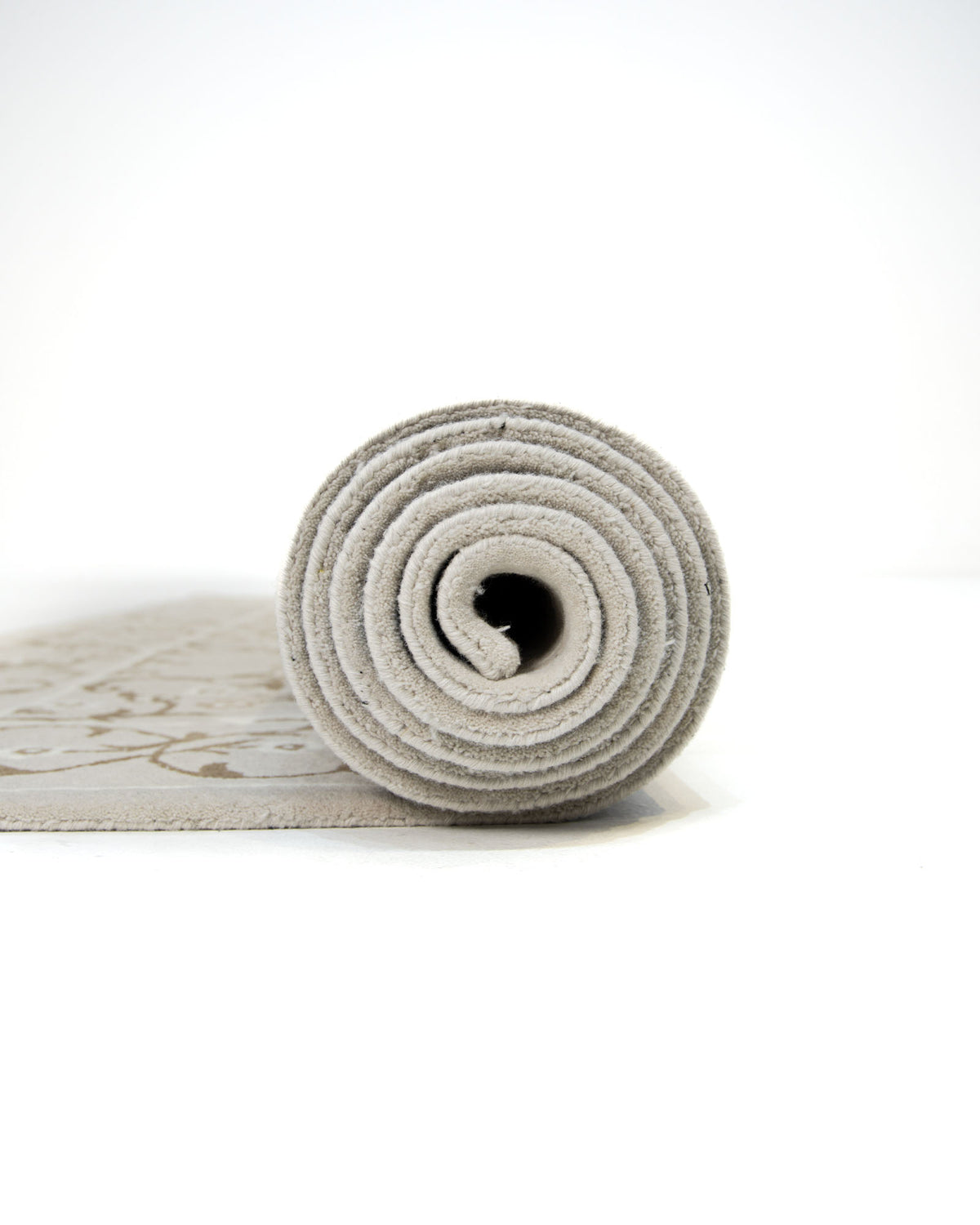 A gray yoga mat is partially unrolled on a white surface, with the rolled end facing the camera and the mat’s faintly visible textured pattern reminiscent of the Exquisite Multi Color Decor Handmade Rug - HTW 99 (300x400 CM) by RAMSHA HOME.