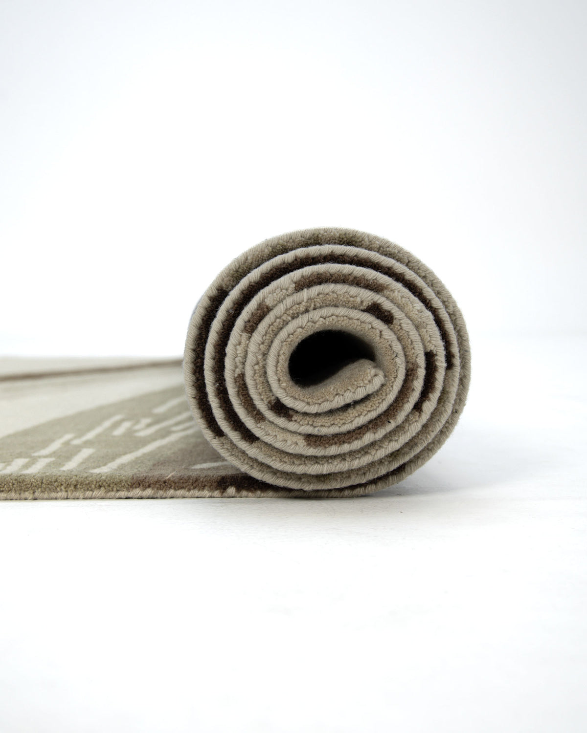 A Striking Pattern Home Decor Handmade Carpet (HTW-61) by RAMSHA HOME in beige is tightly rolled up on a white surface, viewed from the side to clearly showcase the spiral pattern of the roll.