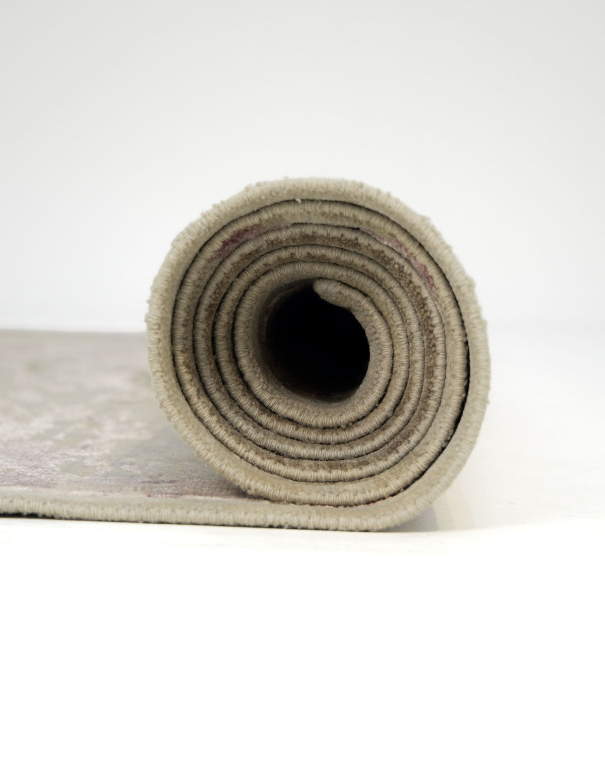 A close-up view of the RAMSHA HOME Hand Knotted Living Room Rug - HKWV-03 (240x300 CM), rolled up to display its beige silk wool layers, placed on a white surface against a plain white background.