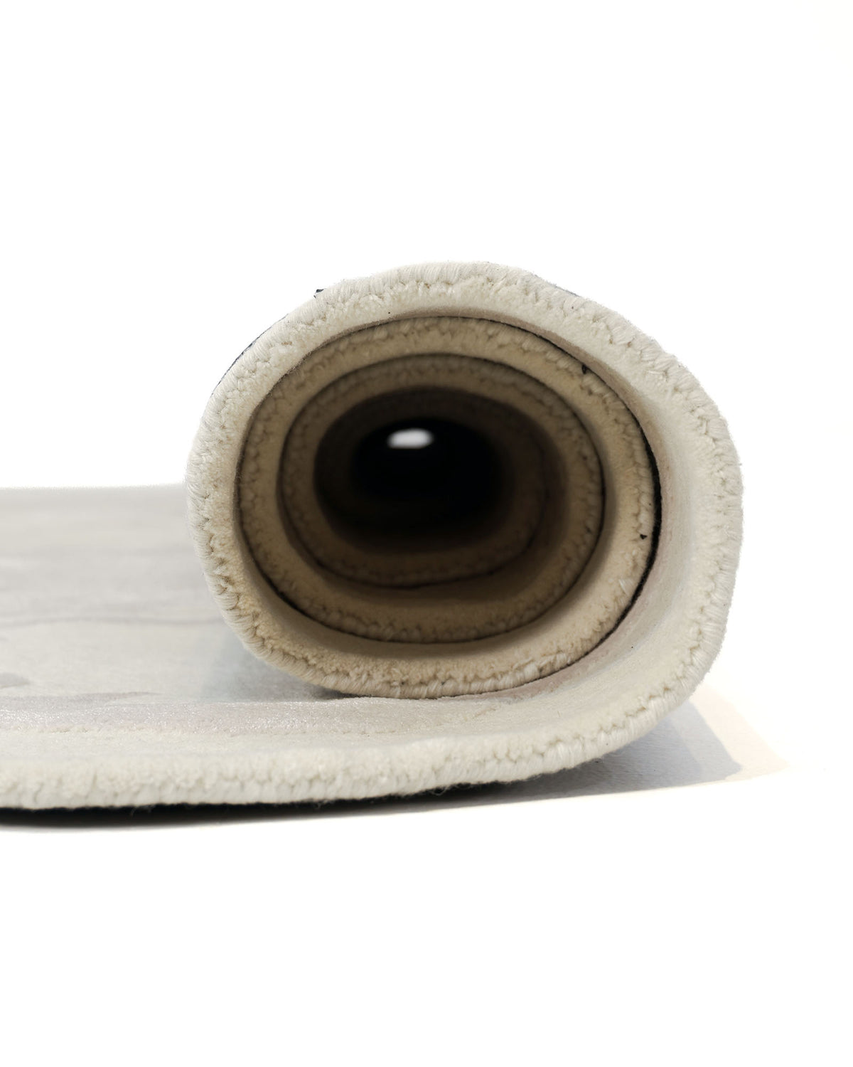 A close-up view of the RAMSHA HOME Abstract Beige Handcrafted Rug – Neutral Textured Modern Area Rug (HTWV 205), rolled up and photographed from the end, reveals its circular layers and soft texture against a white background.
