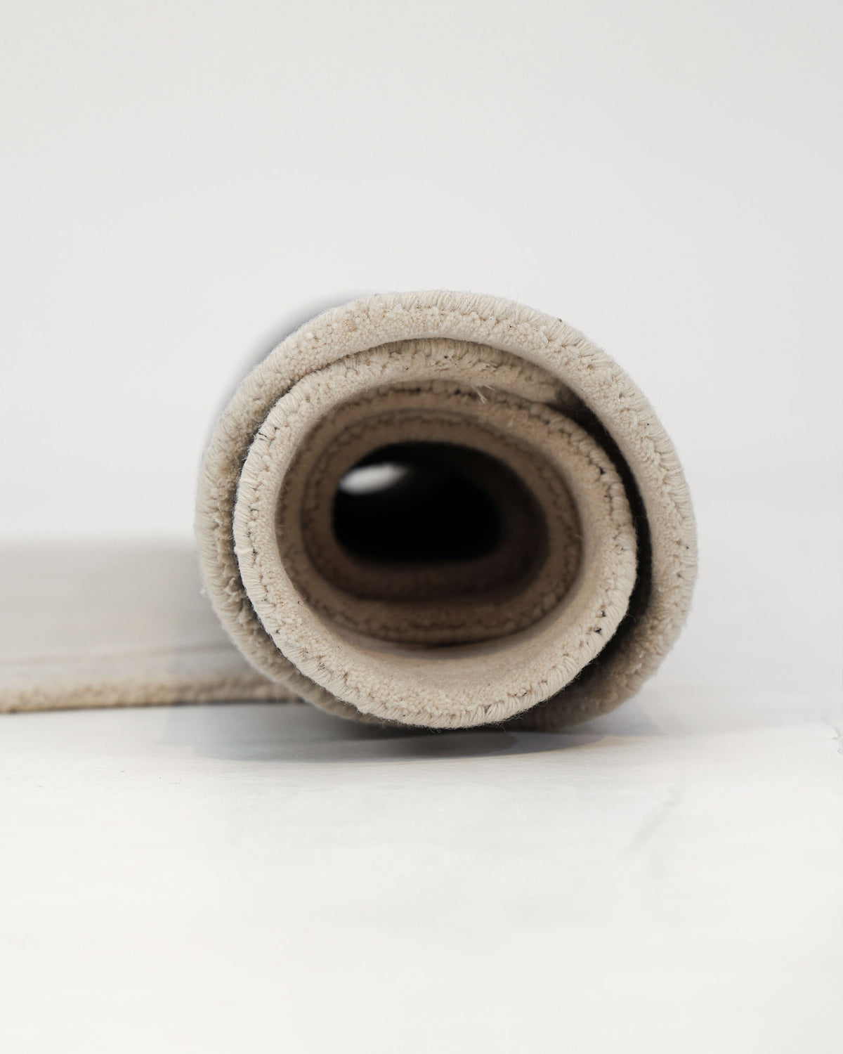 Close-up of a rolled-up RAMSHA HOME Multi Color Handmade Area Rug - HTWV-136 (200x300 cm) on a white surface, highlighting its soft texture and circular layers from a side view.