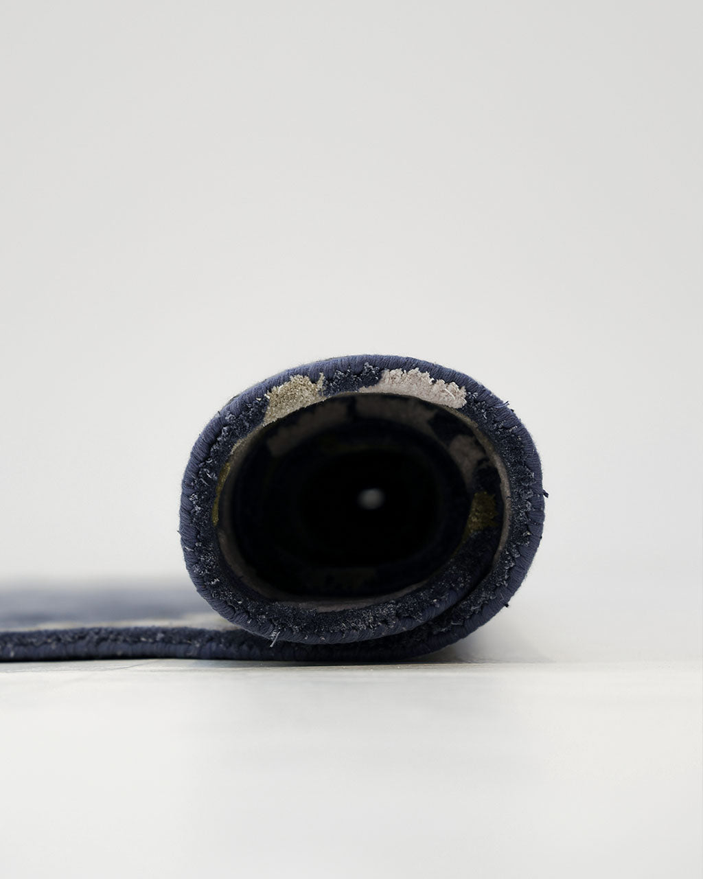 A rolled-up Navy Blue Viscose Shaped Handmade Carpet 200x300 - HTV-23 by RAMSHA HOME stands upright against a plain, light background, displaying the circular layers of its fabric. This hand-tufted piece brings a touch of sophistication to any space.