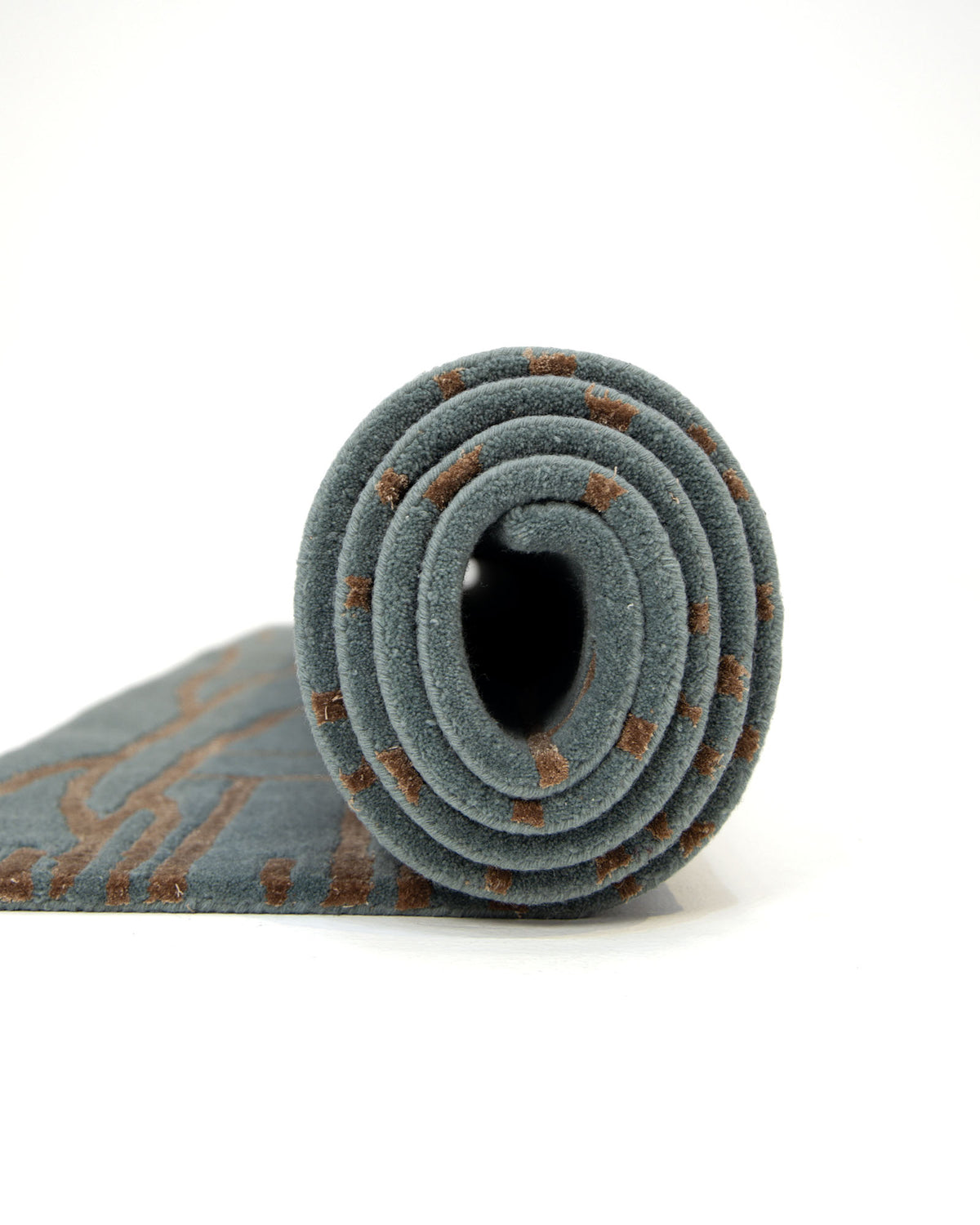 A rolled-up RAMSHA HOME Abstract Rust Line Grid Teal Rug (HTWV-31, 180x270 CM), featuring a hand-tufted design with a brown geometric pattern on a gray background, displayed against a plain white backdrop.
