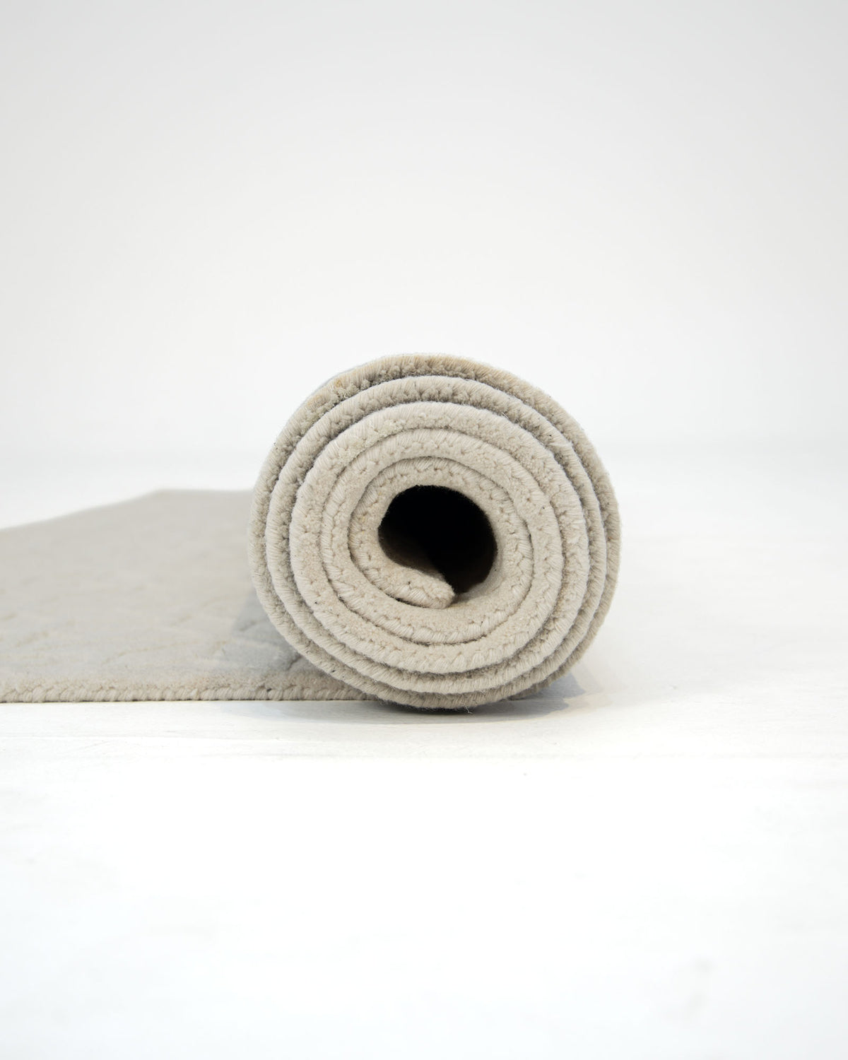 A rolled-up Handmade Beige Color Area Rug - HTWV 165 (200X300 cm) from RAMSHA HOME is displayed on a white surface, with part of the beige, geometric-patterned rug unrolled to the left against a plain, uncluttered background.