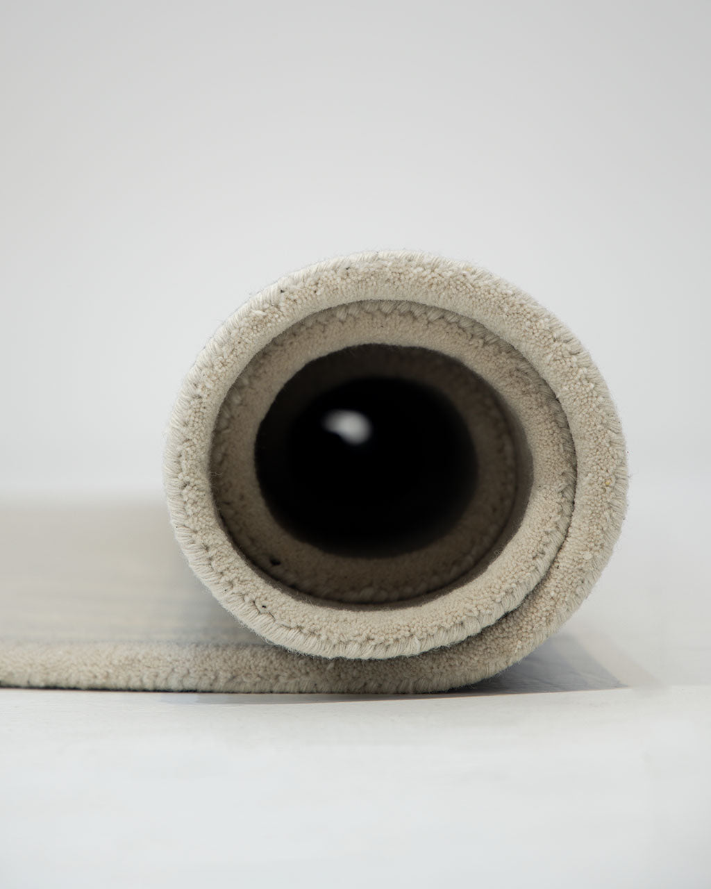 A close-up view of a rolled-up RAMSHA HOME Hand Tufted Beige Color Decor Rug HTWV-108 on a light surface, highlighting the rug’s soft texture and circular shape from the end.