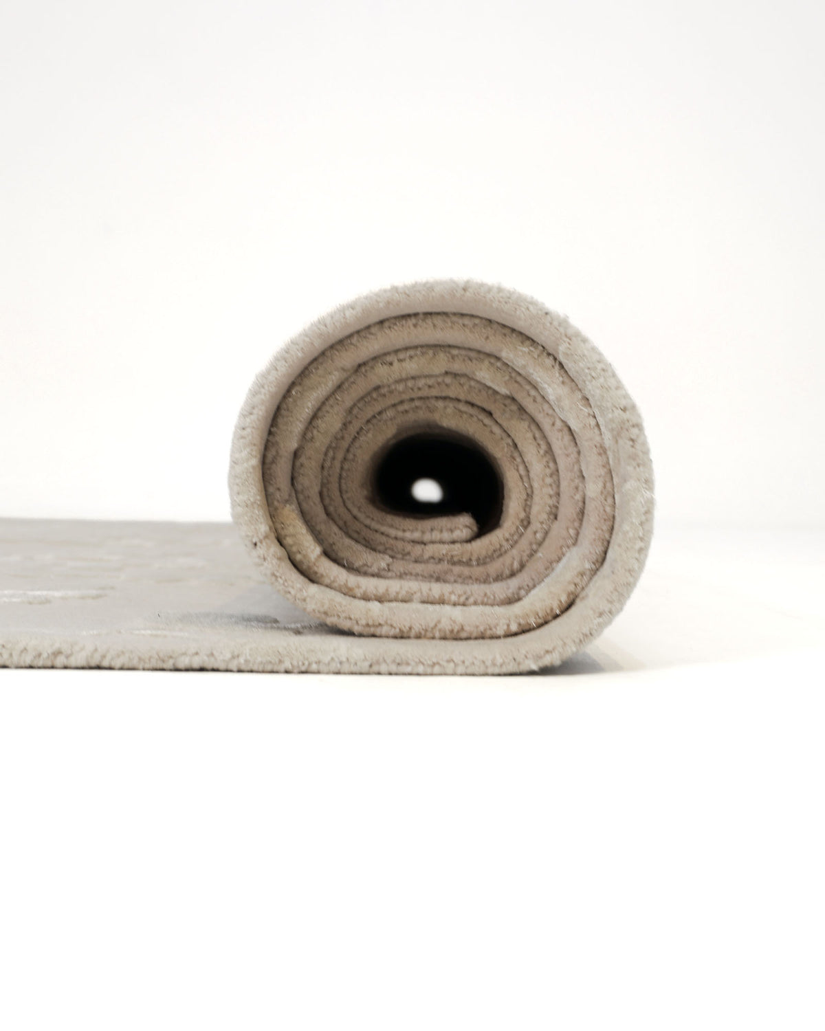 A RAMSHA HOME Artisan Handmade Decorative Area Rug – HTWV-116 with a beige botanical design is tightly rolled up on a white surface, showcasing its spiral pattern from a front-facing perspective.