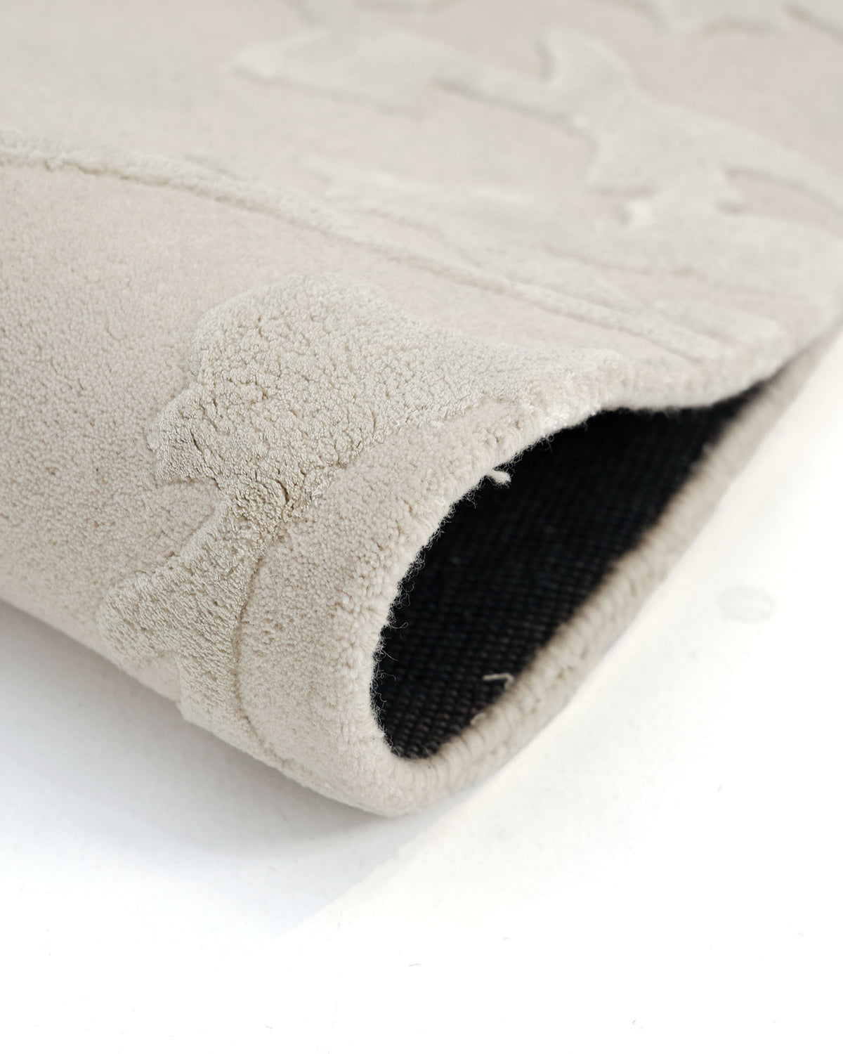 A close-up of the RAMSHA HOME Decorative Handmade Area rug HTWV-118, a beige hand-tufted wool blend rug with animal patterns, shown partially rolled to reveal its dark woven underside.