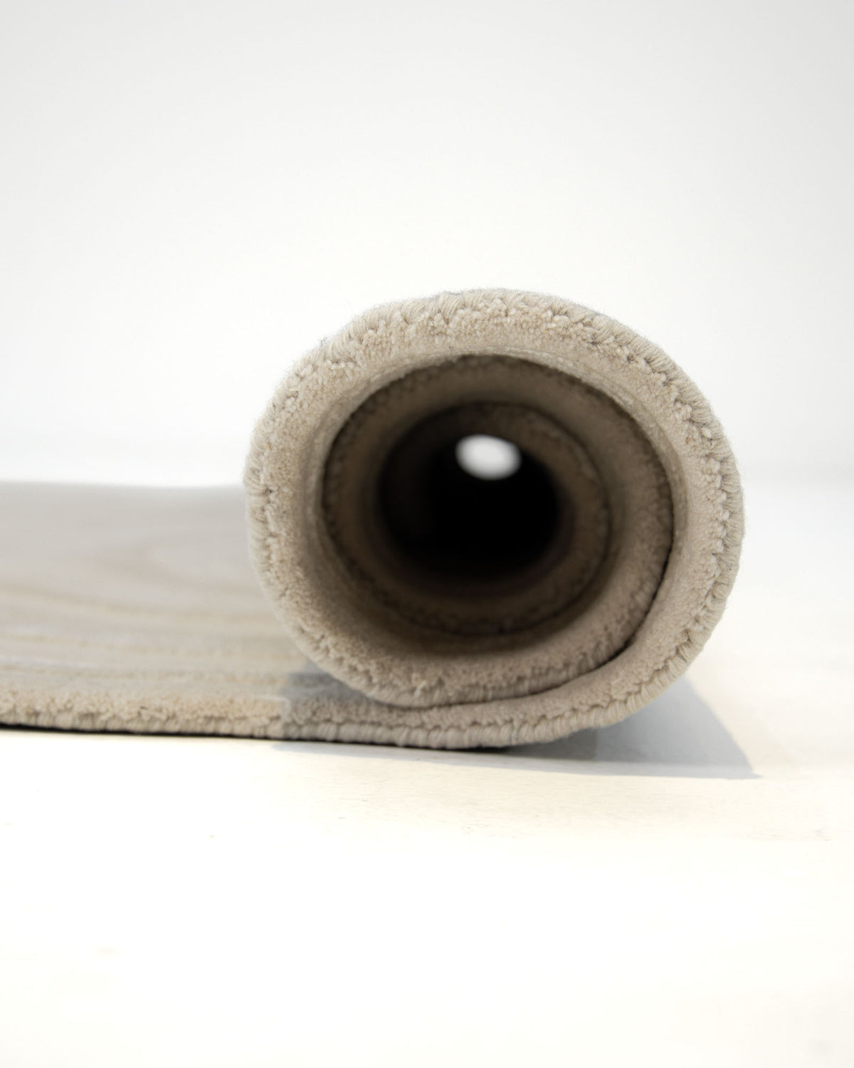 A close-up of the RAMSHA HOME Handmade Beige Organic Shape Rug with Wave Pattern 200x300 cm – HTWV 210, featuring its soft textured surface and rolled end facing the camera, displayed on a white background.