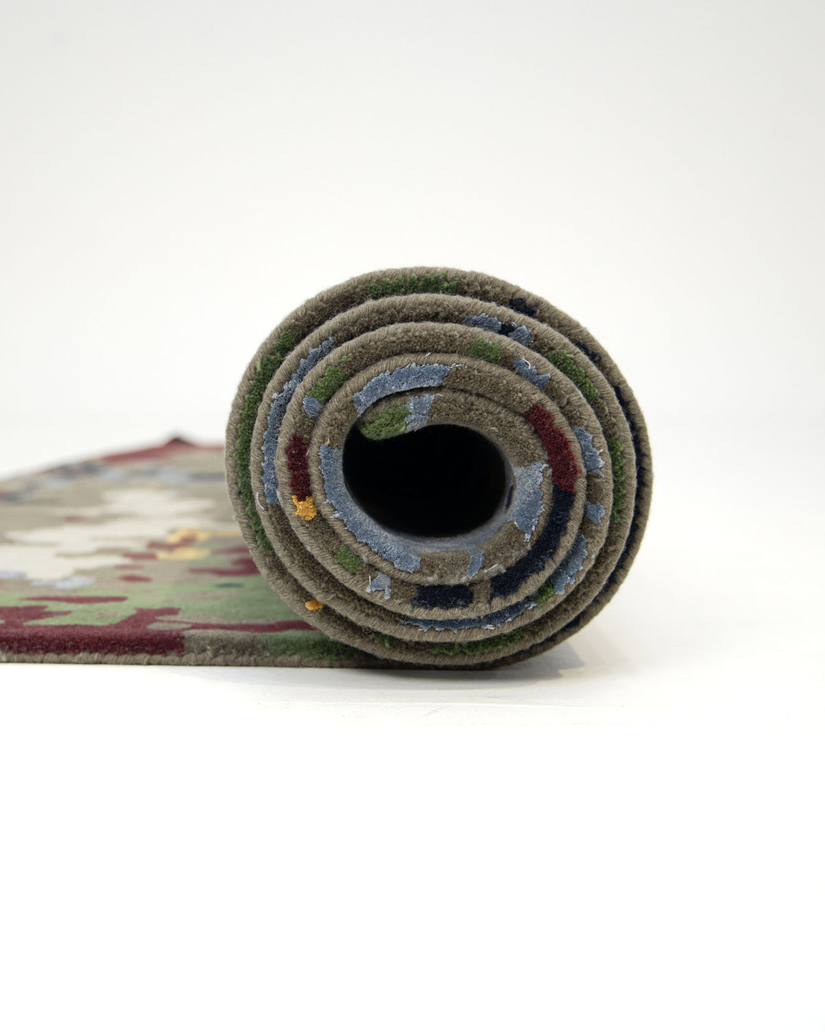 A close-up of the RAMSHA HOME Modern Artistic Handmade Rug 240x300 cm - ZUA-21, rolled up and standing upright on a plain white surface, reveals its colorful, textured edge and striking geometric design.