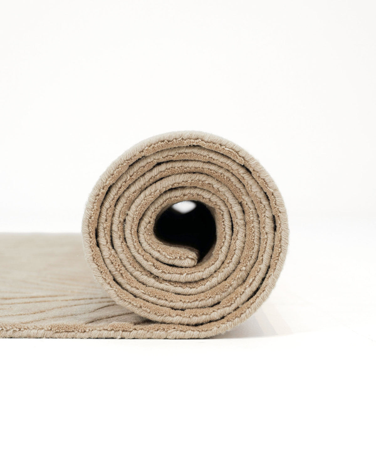 The RAMSHA HOME Decorative Handmade Beige Color Area Rug (LKH-028) is shown tightly rolled from one end, highlighting its spiral pattern against a plain white background.