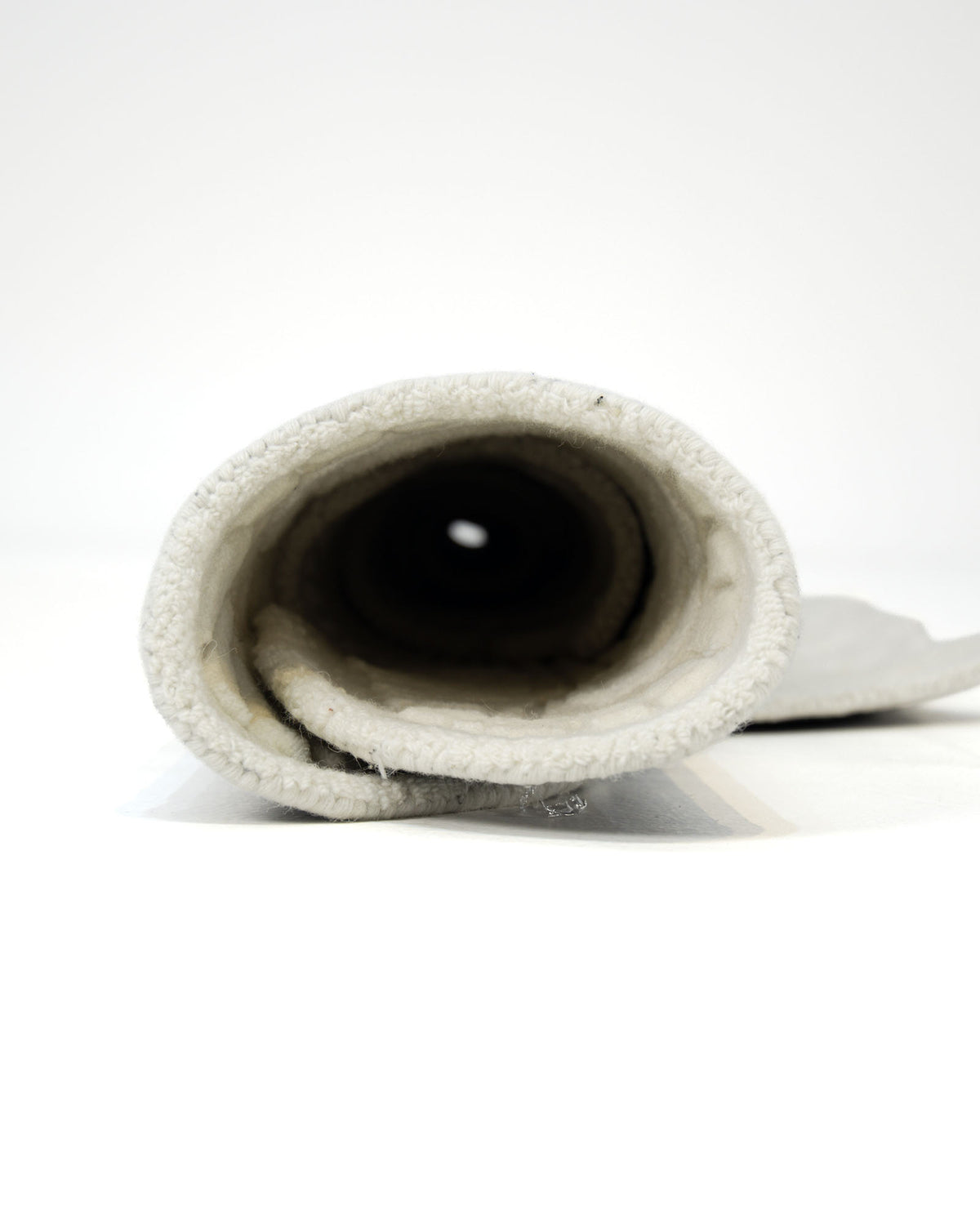 A rolled-up white towel with a soft, textured surface, viewed from one open end against a plain white background, evokes the cozy comfort of the RAMSHA HOME Natural Handmade Area Rug (HTWV-126).