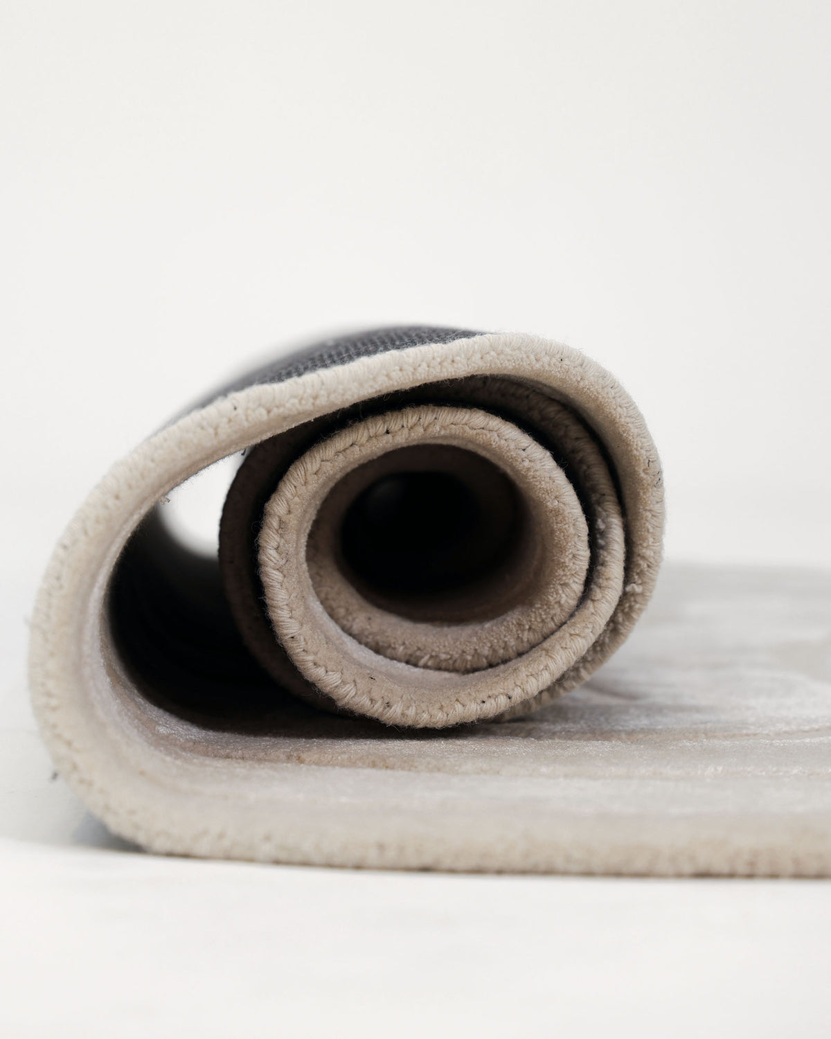 A close-up side view of the RAMSHA HOME Luxurious Off-White Hand-Tufted Rug - HTWV 111 (200x300cm) showcases its soft, plush texture, revealing the inner layers and edge stitching against a plain white background.