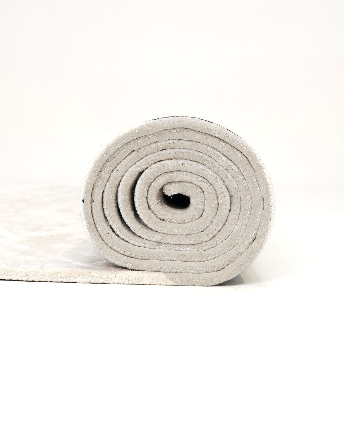 A close-up of a rolled-up RAMSHA HOME Beige Color Indoor Handmade Area Rug - HTV 15 on a white background, with the spiral pattern of the rug clearly visible from the side.
