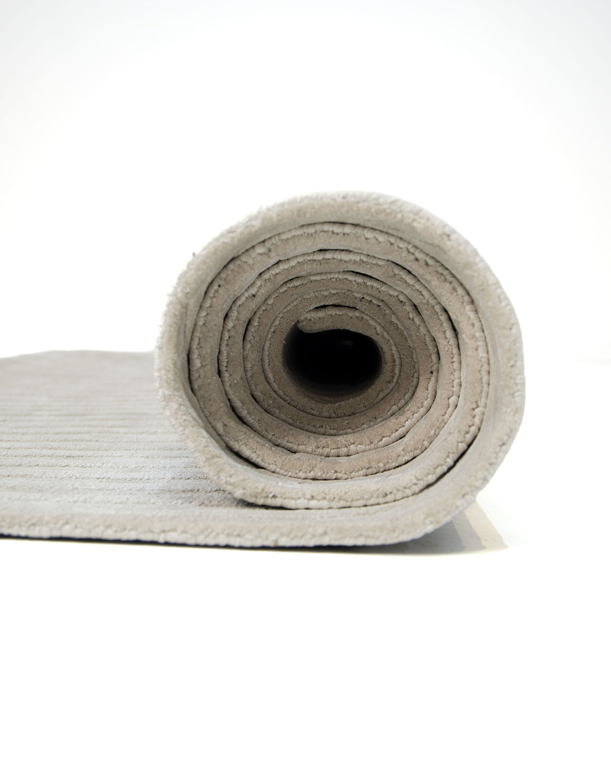 A close-up view of the RAMSHA HOME Off White Handmade Rug - HTV 14, rolled up on a white background, highlights its modern textured surface and spiral pattern, showcasing the rug’s soft fabric.
