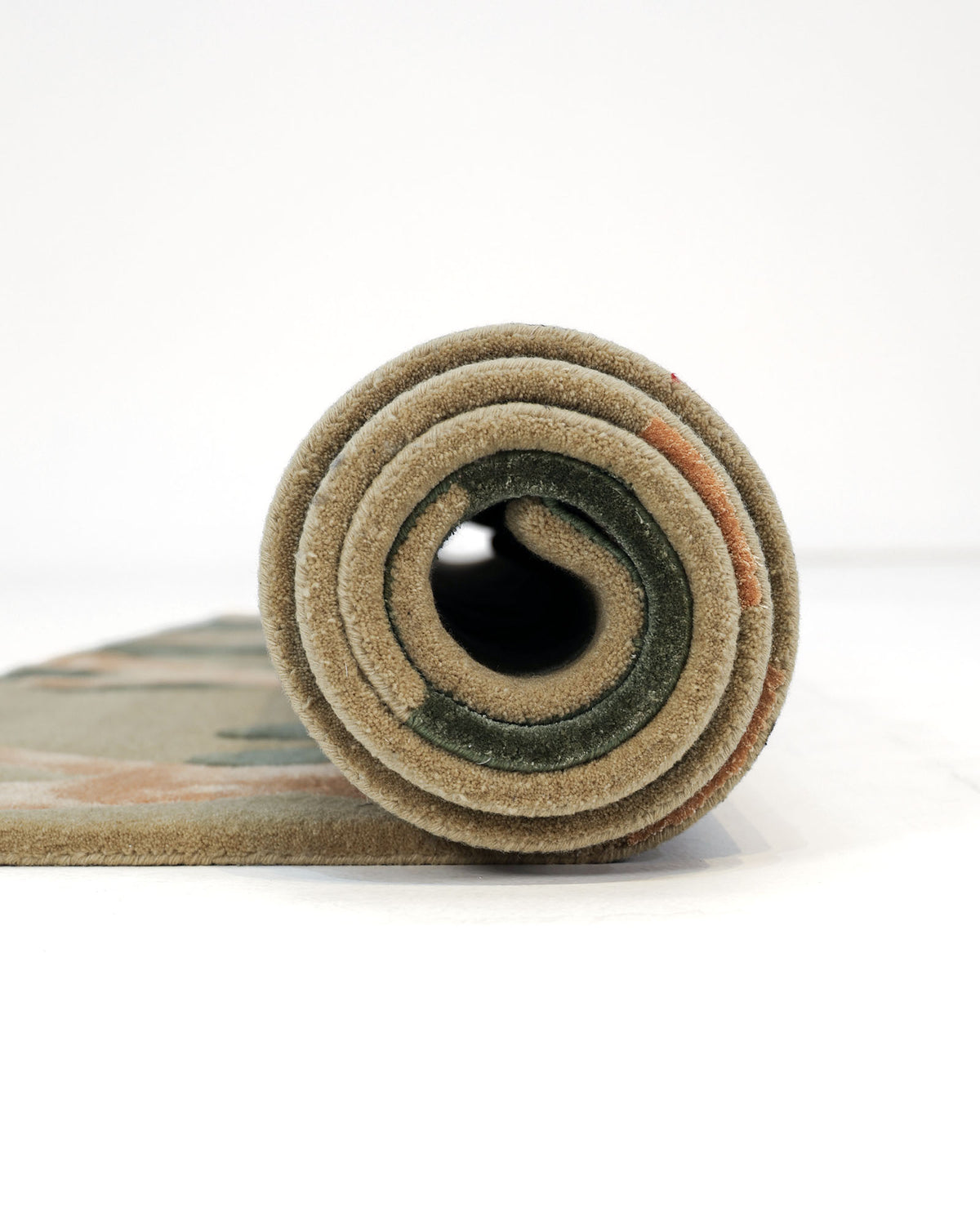 A rolled-up RAMSHA HOME Sage Green & Beige Contemporary Designer Rug (180x270 cm, HTWV 22) is viewed from the side, displaying concentric circles of thick, textured fabric in sage green and beige hues against a plain white background.