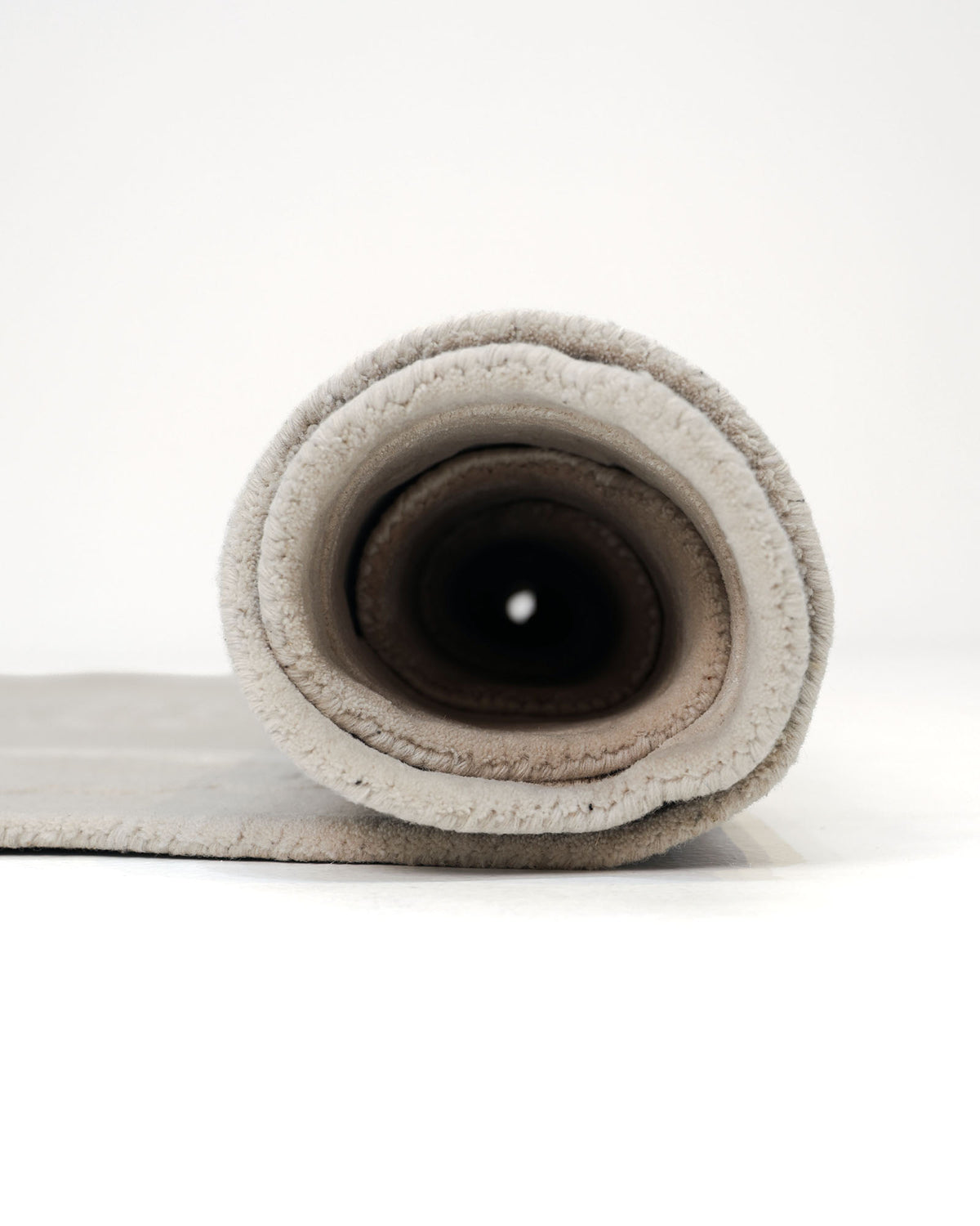 A close-up view of a rolled-up light gray yoga mat on a white surface, with its textured edges and hollow center facing the camera, placed next to the Abstract Beige Handcrafted Rug – Neutral Textured Modern Area Rug– HTWV 204 by RAMSHA HOME, which subtly complements the minimalist setting.