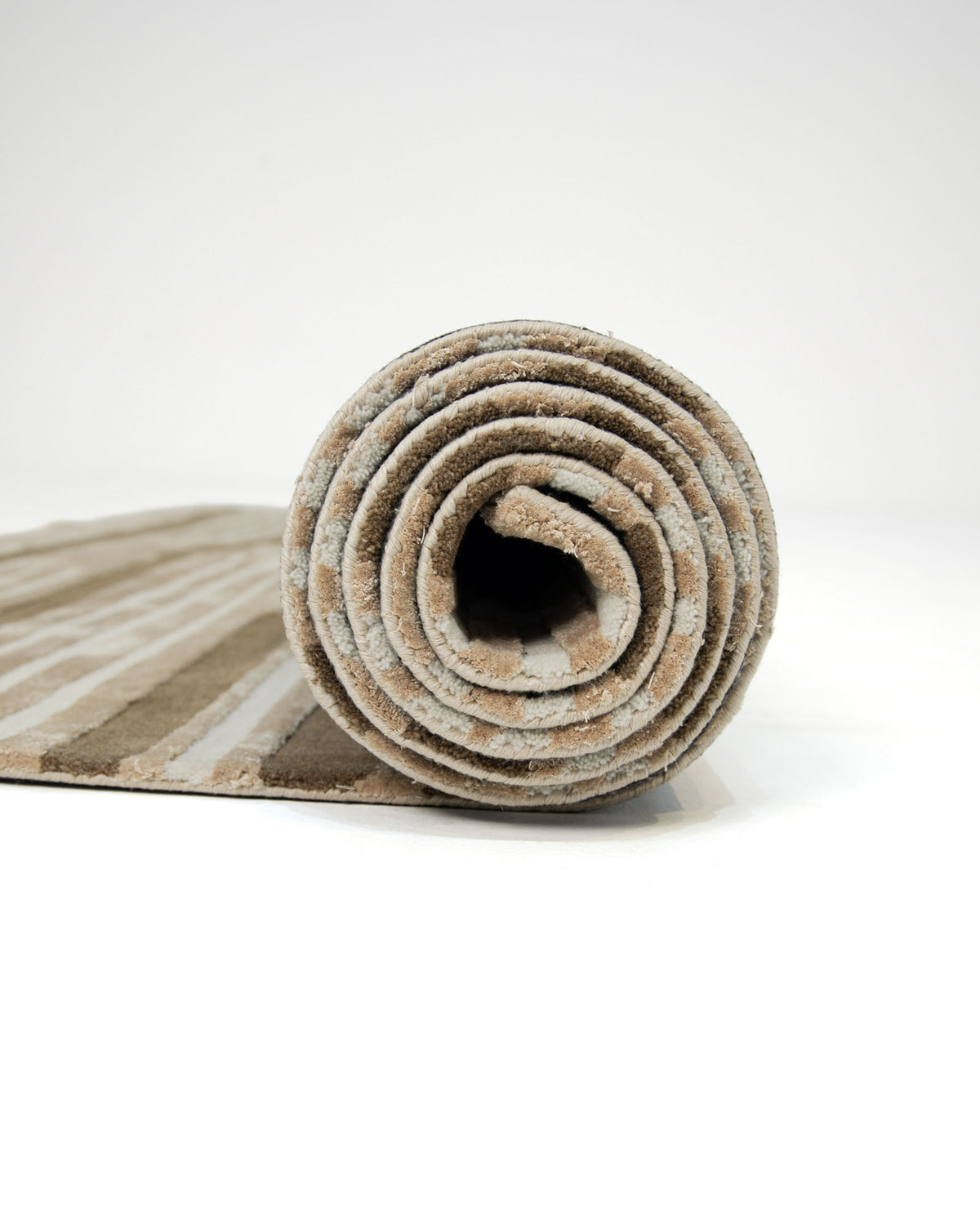 A rolled-up Amazing Multi Color Bedroom Floor Rug - ZUA 13 (250x350cm) by RAMSHA HOME, featuring modern beige and light gray stripes, is placed on a white surface with the rolled end facing the camera.