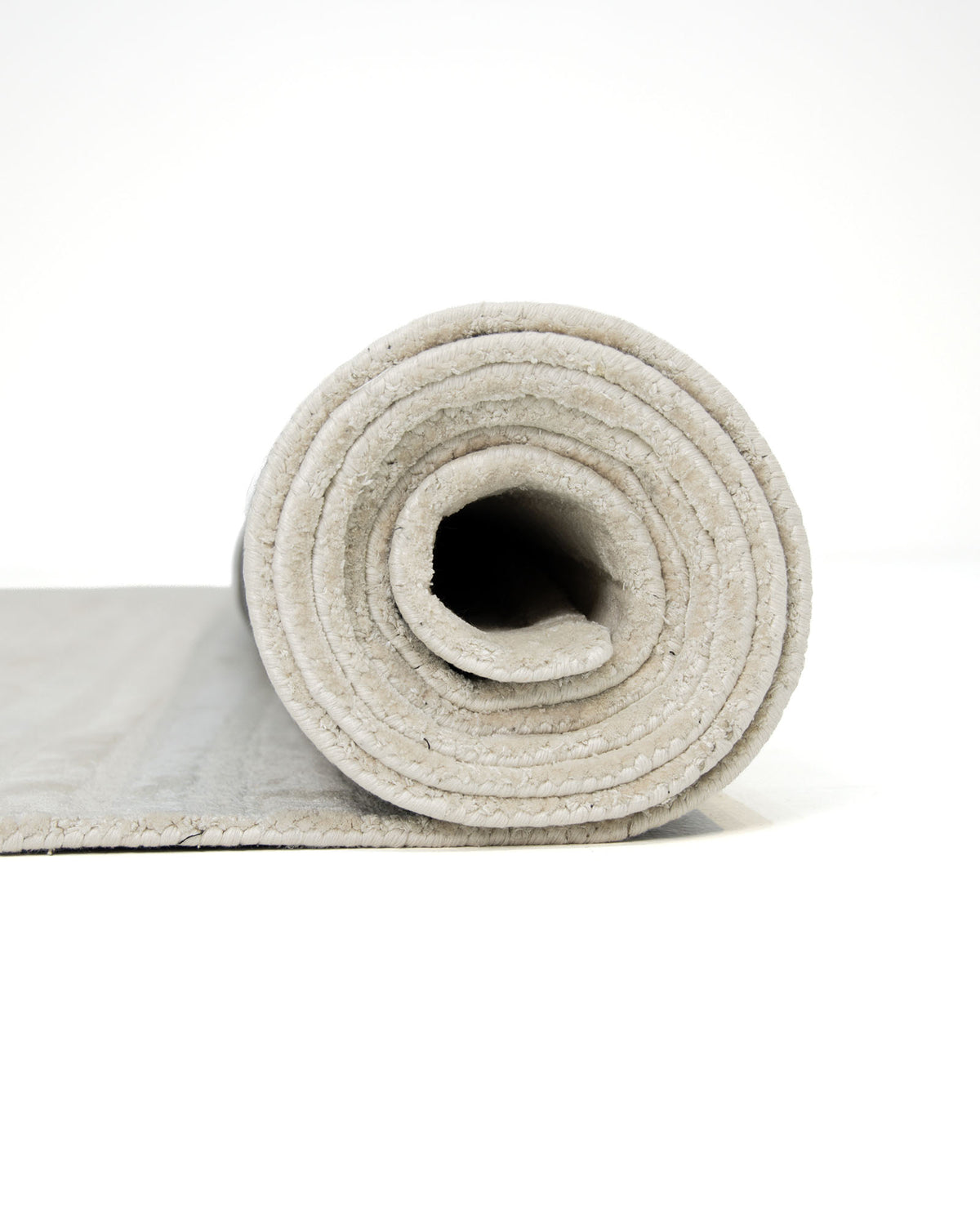 A close-up of the RAMSHA HOME Home Decor Handmade Area Rug - HTV 17, featuring a rolled-up, light beige, neutral textured design on a white background, with part of the rug unrolled and lying flat.