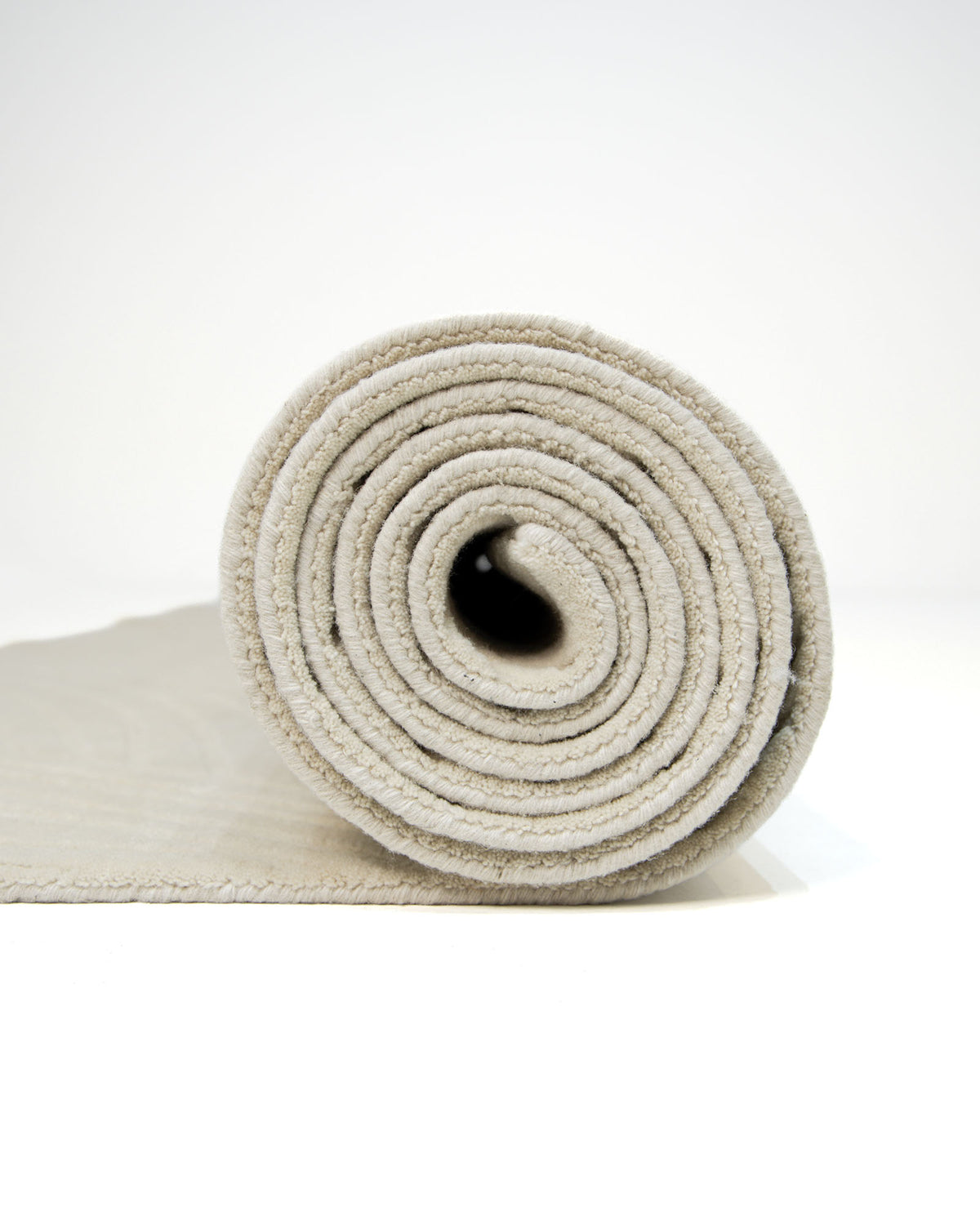 A rolled-up Decorative Rectangle Handmade Beige Color 300x400 cm Area Rug by RAMSHA HOME (LKH-033), evoking modern simplicity, is shown standing on its end with part of the rug unrolled and lying flat on a white surface against a plain white background.