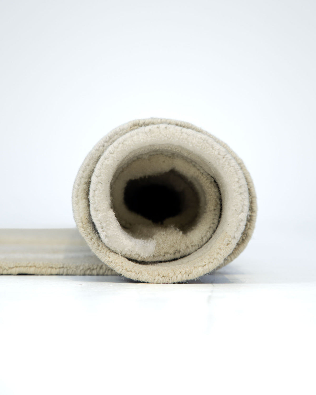 A rolled-up Handcrafted Natural White Area Rug – HTWV-129 by RAMSHA HOME stands upright on a white surface, viewed from the front to reveal the circular layers of the carpet.