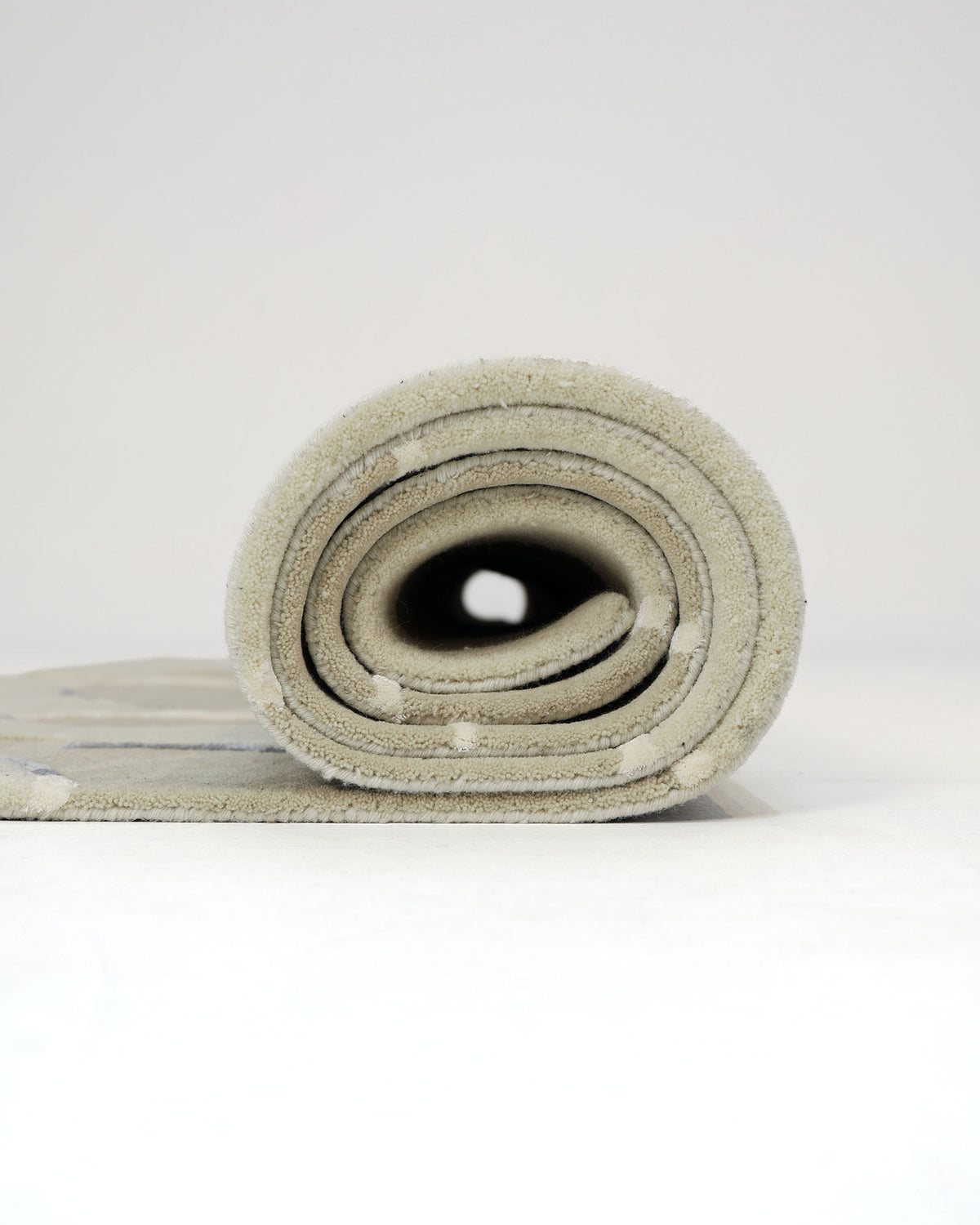 A close-up of a rolled-up RAMSHA HOME Abstract Multi-Tone Handmade Carpet – HTWV-175 (200x300 cm) on a white surface, viewed from the side, revealing its spiral layers and soft texture—echoing the sophisticated appeal of modern design.