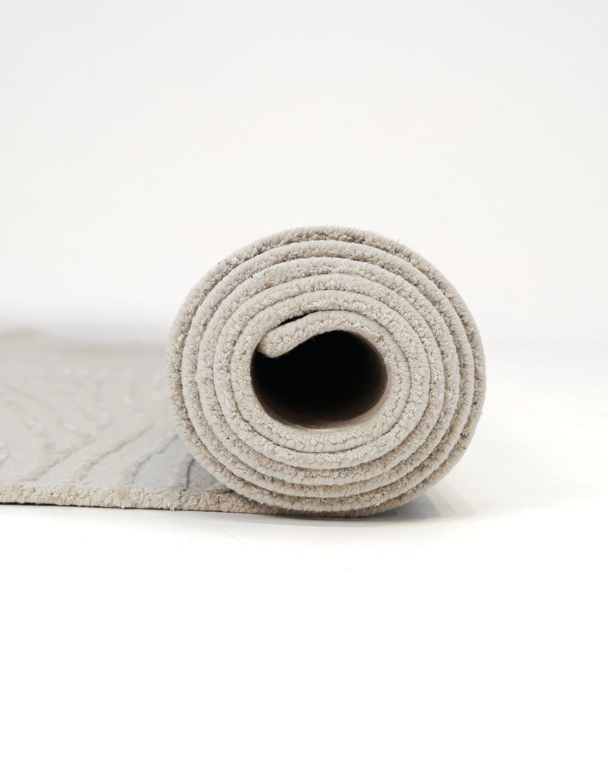 A rolled-up RAMSHA HOME Natural White Color Handmade Area Rug - HTWV-143 (300x400 cm) is partially unrolled on a white surface, revealing its textured design and prominent spiral pattern in a light natural white shade, as seen from the side.