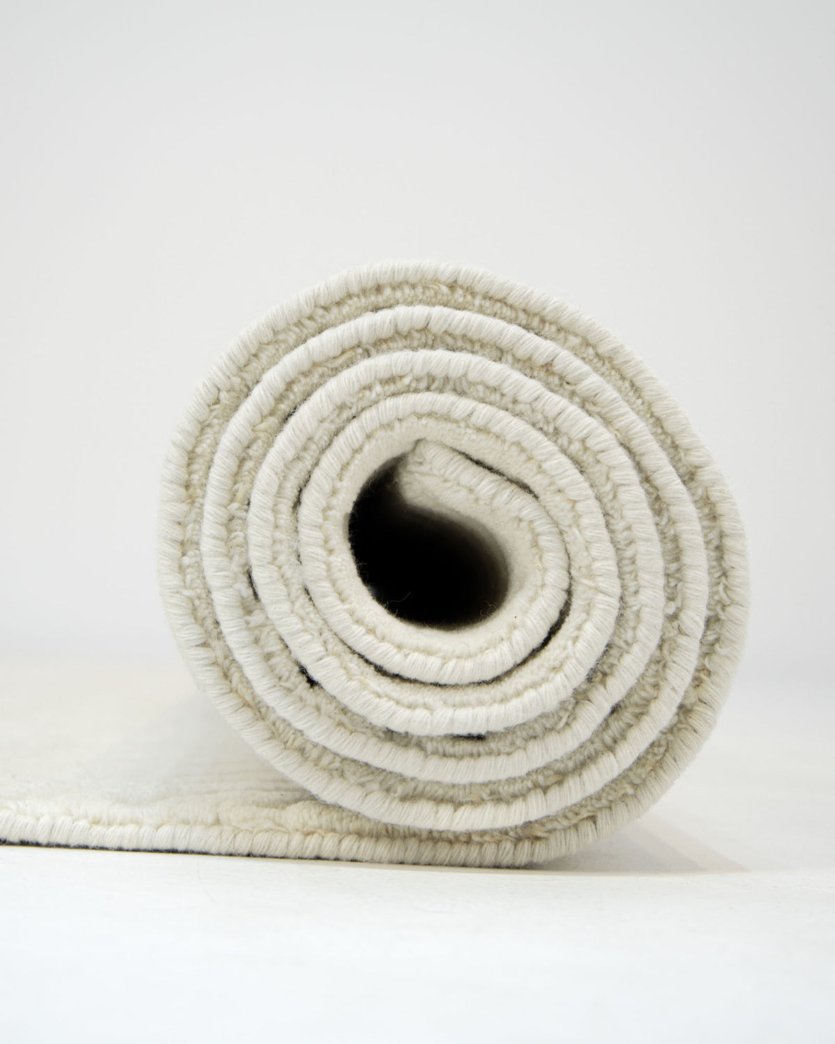 A close-up view of the RAMSHA HOME Natural Color Handmade Area Rug - LKH-018 (200x300 cm), rolled up to reveal its concentric layers and textured edges in light beige, set against a plain white background.