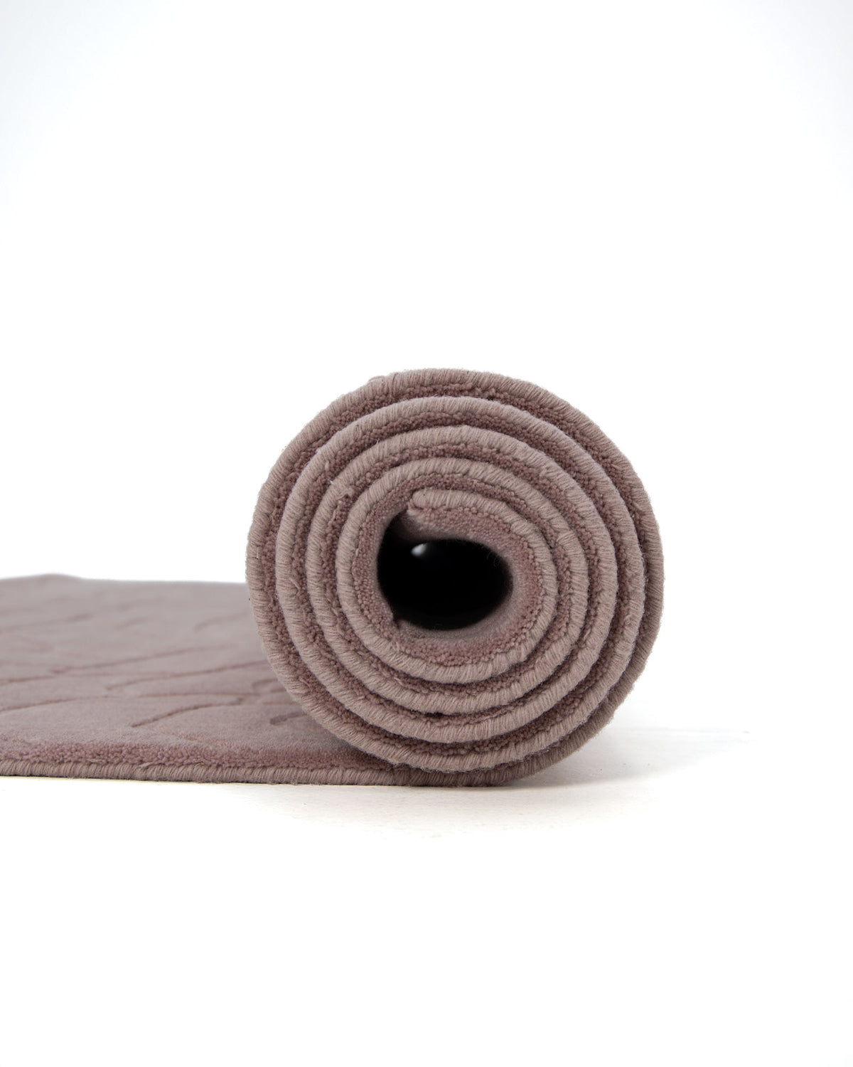 A mauve-colored yoga mat is rolled up on a white background, its spiral pattern clearly visible—a soft hue reminiscent of the Rectangle Handmade Pink Color Area Rug (LKH-029) by RAMSHA HOME.