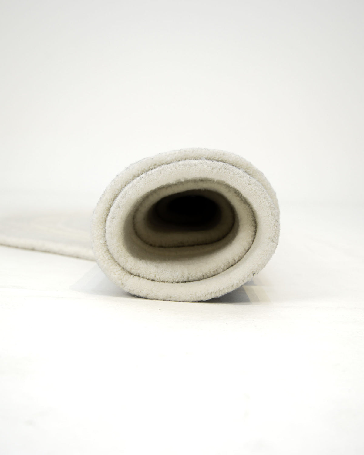 A close-up view of the RAMSHA HOME Ivory Topographic Shaped Rug (200x300 cm, Rug HTWV-192) showcases its sleek and understated elegance, rolled up and photographed from one end against a plain white background.