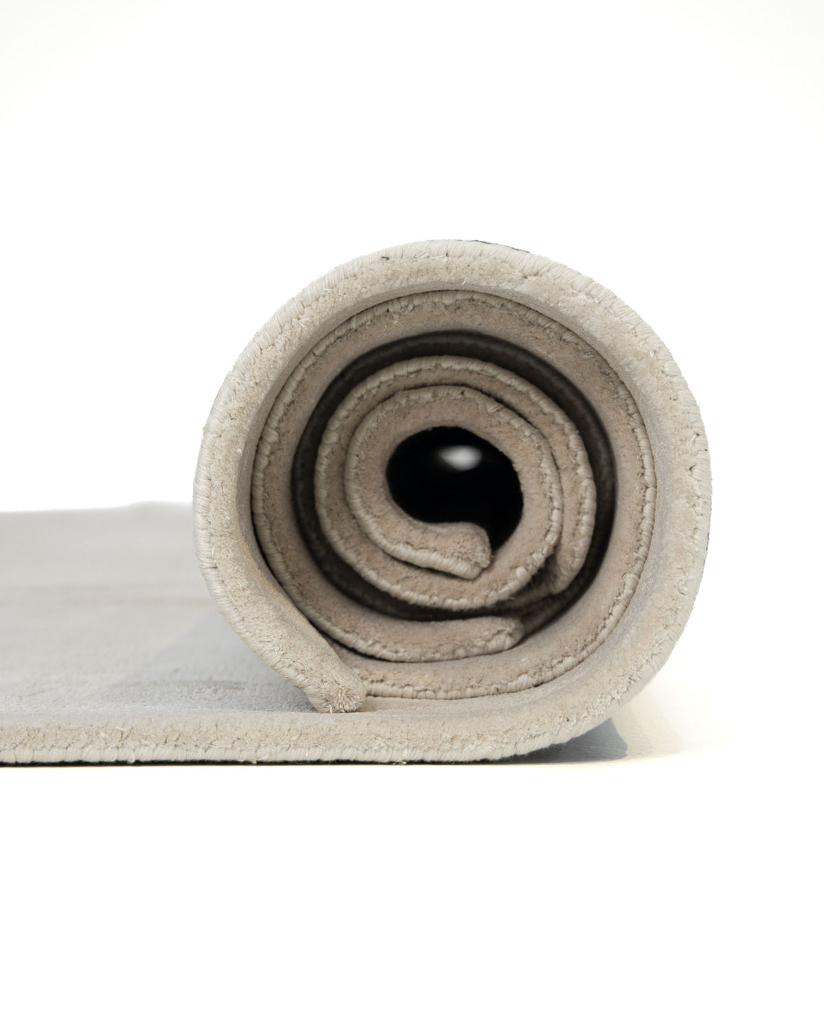 A close-up of a gray yoga mat rolled up tightly, viewed from the side with its spiral layers against a white background—perfectly complementing the clean lines and soft tones of the RAMSHA HOME Modern Viscose & Wool Handmade Carpet 200x300 (HTWV-172), bringing tranquility to any calming space.