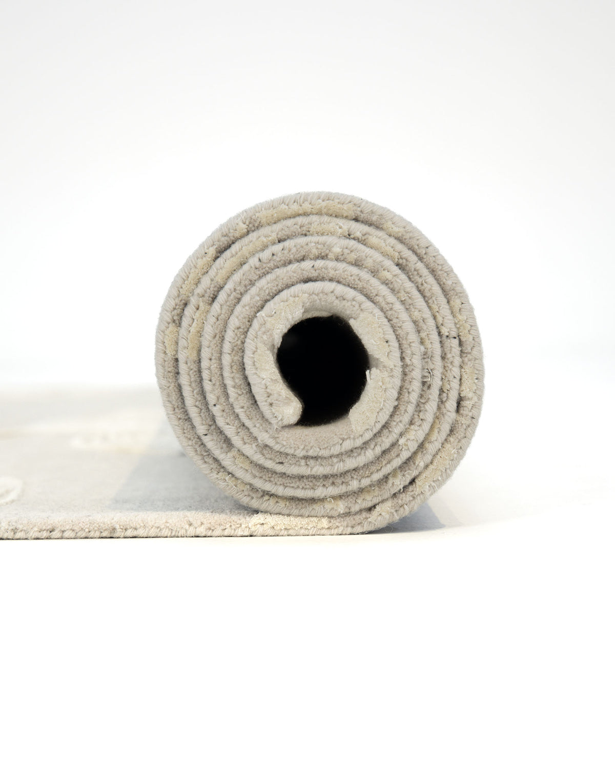 A rolled-up Natural Beige & Ivory Handmade Area Rug - HTWV-146 by RAMSHA HOME is viewed from the side, revealing concentric circular layers and a hollow center, its soft wool texture displayed against a white background.